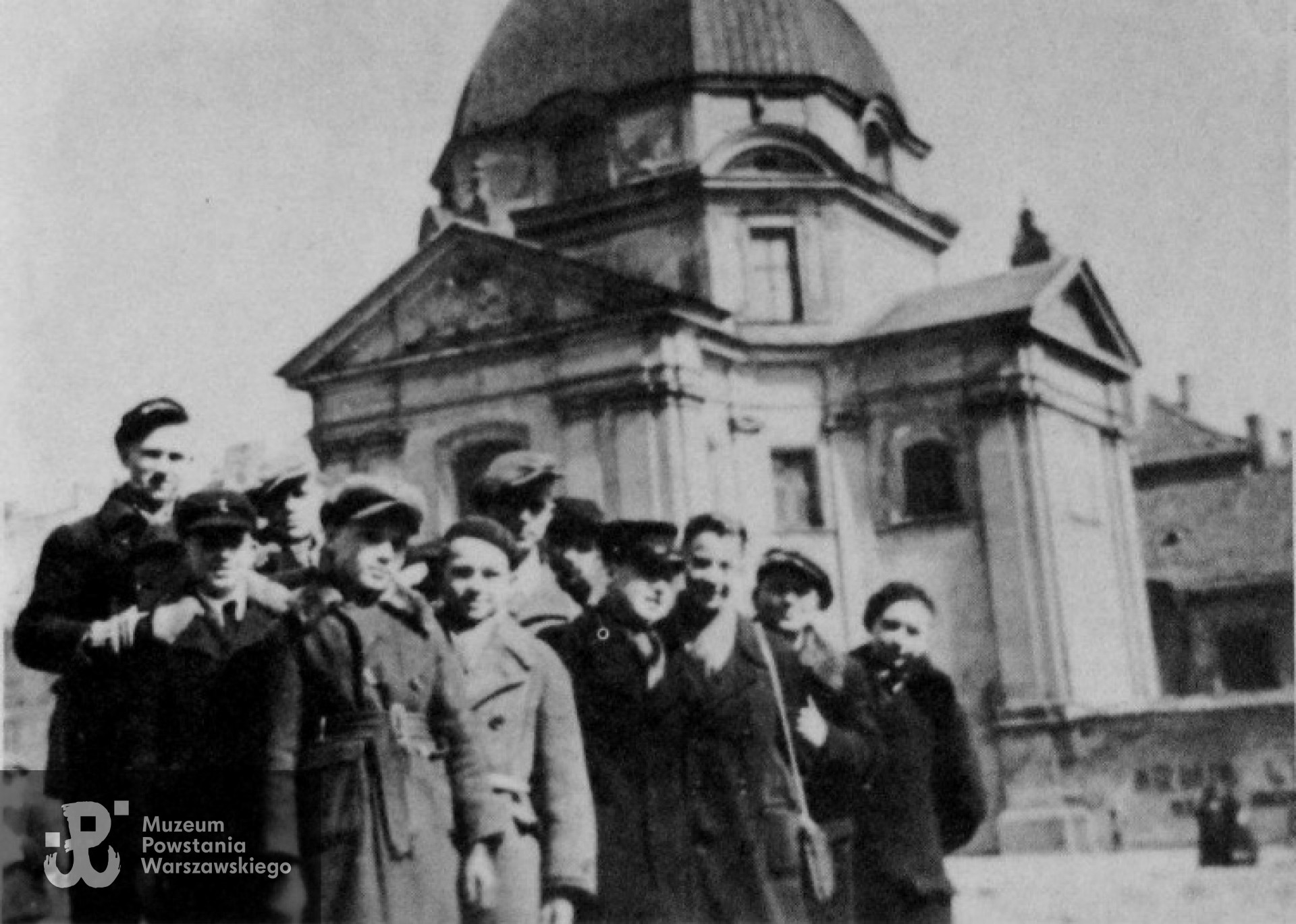 Polne kwiaty 1944 : dotychczas niepublikowane pamiątkowe zdjęcie grupy harcerzy "Szarych szeregów" wykonane w kwietniu 1944 na Nowym Mieście w Warszawie. Chłopcy z Żoliborza złożyli pod murem kościoła św. Kazimierza (Sakramentek) kwiaty polne w następnym dniu po egzekucji mieszkańców Starego Miasta rozstrzelanych przez Niemców. Ten symboliczny gest patriotyczny w ramach "małego sabotażu" mógł kosztować Ich życie. Drugi z prawej Sławek ps. "Bóbr" (pluton 215, Komp. Żbik, Zgr. Żywiciel w Powstaniu Warszawskim) Fotografia wykonana aparatem Kodak Baby Brownie.  Ze zbiorów Sławomira Pocztarskiego.