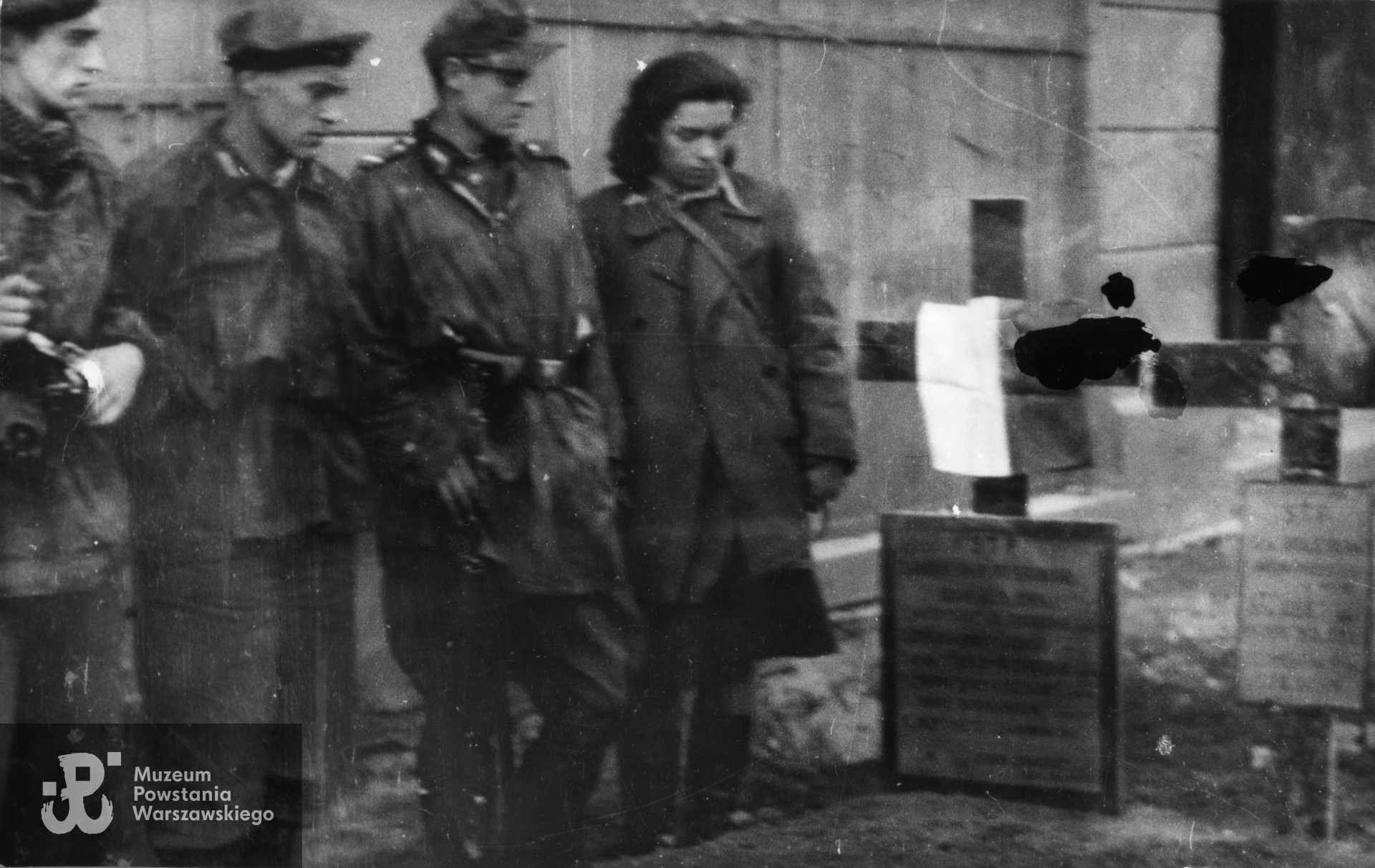 Fotografia z Powstania Warszawskiego. Śródmieście Południowe, ulica Hoża 29, przed kinem "Urania". Powstańcy z Kompanii Ochrony Kwatery Głównej Okręgu Warszawskiego AK przy mogiłach poległych 16 września. Stoją od lewej: ppor. Stanisław Kordzik "Kujawiak", strz. Jerzy Pensiek "Jawa", kpr. Tadeusz Mikulik "Wit", łączniczka i sanitariuszka Maria Kamecka "Jola" (po mężu Kordzik). Fot. ze zbiorów Muzeum Powstania Warszawskiego, sygn. MPW-IK/2858.Ujęcie tożsame MPW-IP/5725.