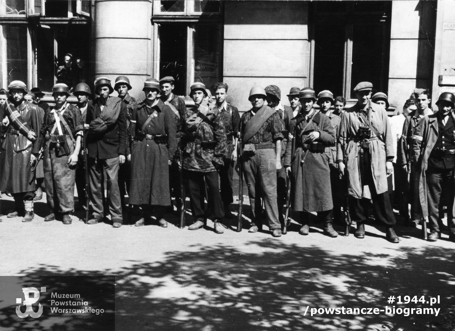 Fotografia z Powstania Warszawskiego. Zbiórka kompanii "Janusz" Batalionu "Harnaś" w podwórzu domu przy ulicy Mazowieckiej 4. W pierwszym szeregu stoją od lewej: ppor. Stanisław Wysocki "Ryszard", plut. pchor. Józef Kowalczyk "Łoś", Jerzy Tomaszewski "Jur", plut. pchor. Zdzisław Surawski "Robinson", NN, strz. "Marynarz", NN, plut.pchor. Adam Podkóliński "Michał", "Olszewski" (z lornetką), NN. Fot. Ze zbiorów Muzeum Powstania Warszawskiego, sygn. MPW-IK/2706