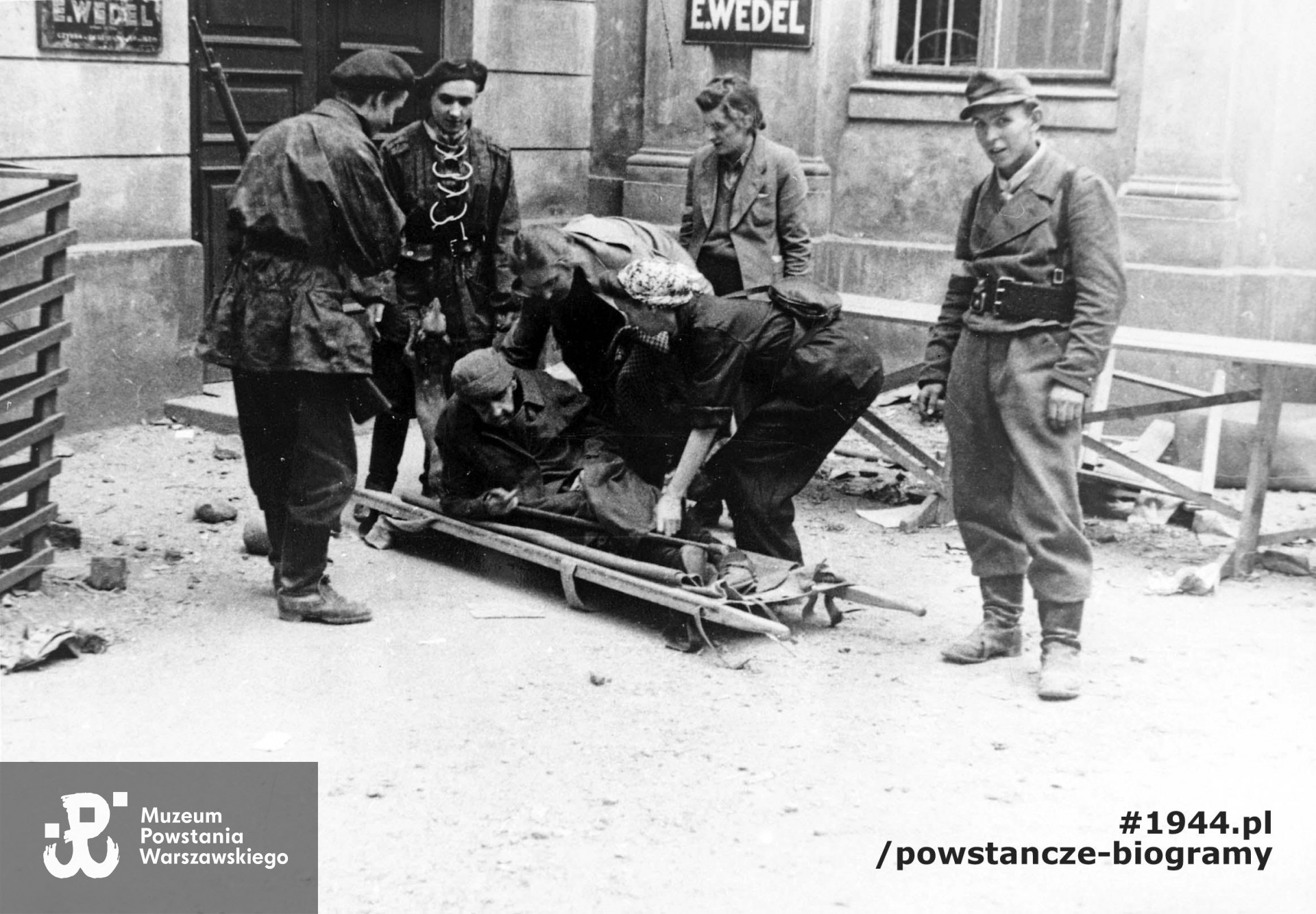 Fotografia wykonana podczas Powstania Warszawskiego. Śródmieście Północne. Patrol sanitarny z III Zgrupowania "Konrad" przed sklepem "Wedla", przy ul. Szpitalnej 8, podczas ewakuacji pisarki Marii Rodziewiczówny. Autorem zdjęcia jest Antoni Bohdziewicz. Fot. ze zbiorów Muzeum Powstania Warszawskiego, sygn. MPW-IP/3201