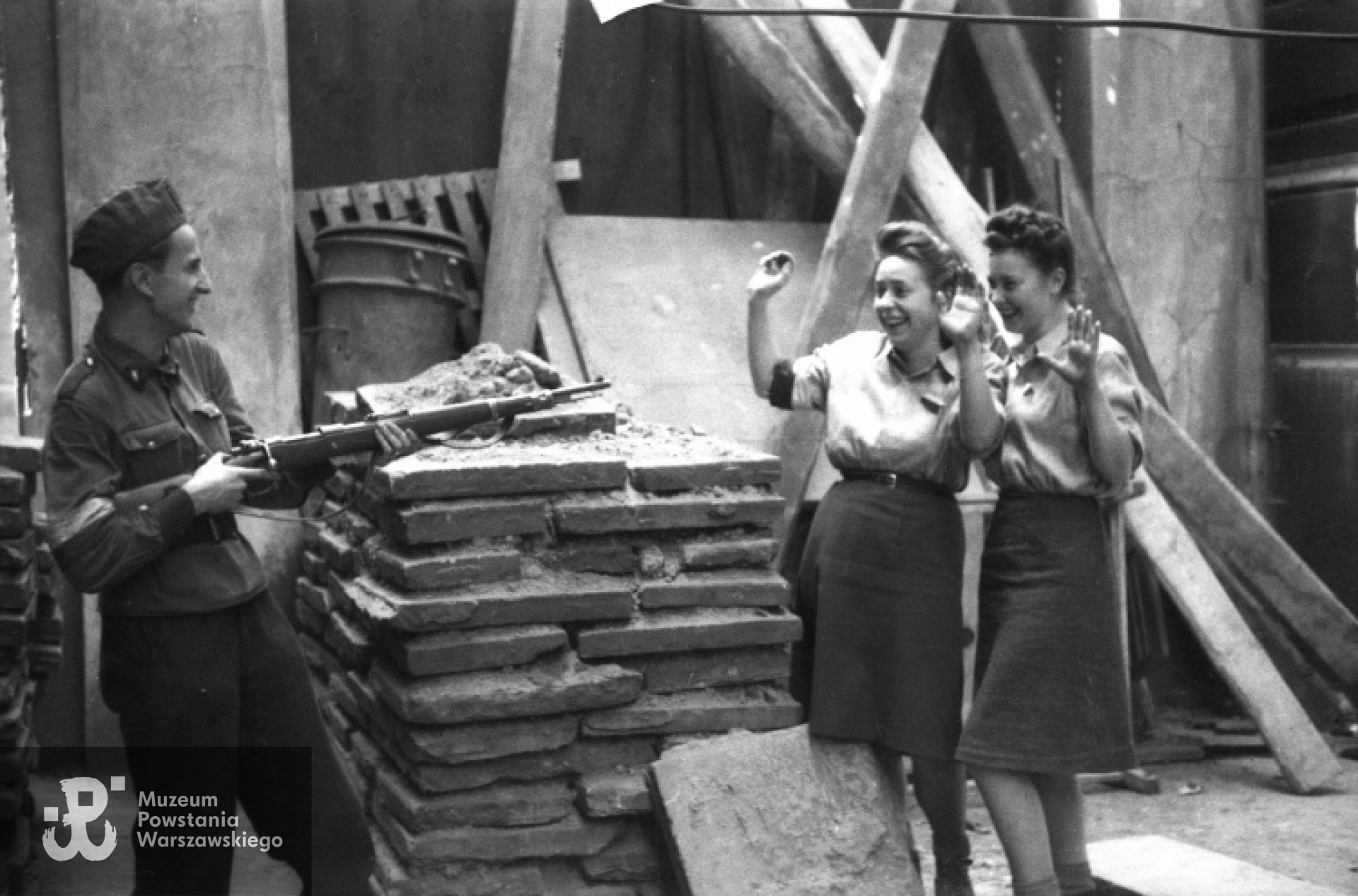 Sierpień 1944 roku. Od prawej łącz. Halina Kenska "Marzena" i sanit. Irena Woźniak "Ewa", obie z 4 komp. "Odwet" Batalionu "Golski, pozują do zdjęcia przed żołnierzem trzymającym karabin. Fot. Andrzej Bargiełowski "Stańczyk". Ze zbiorów Fototeki Muzeum Powstania Warszawskiego, sygn. MPW-IN/882, prawa autorskie: MPW.