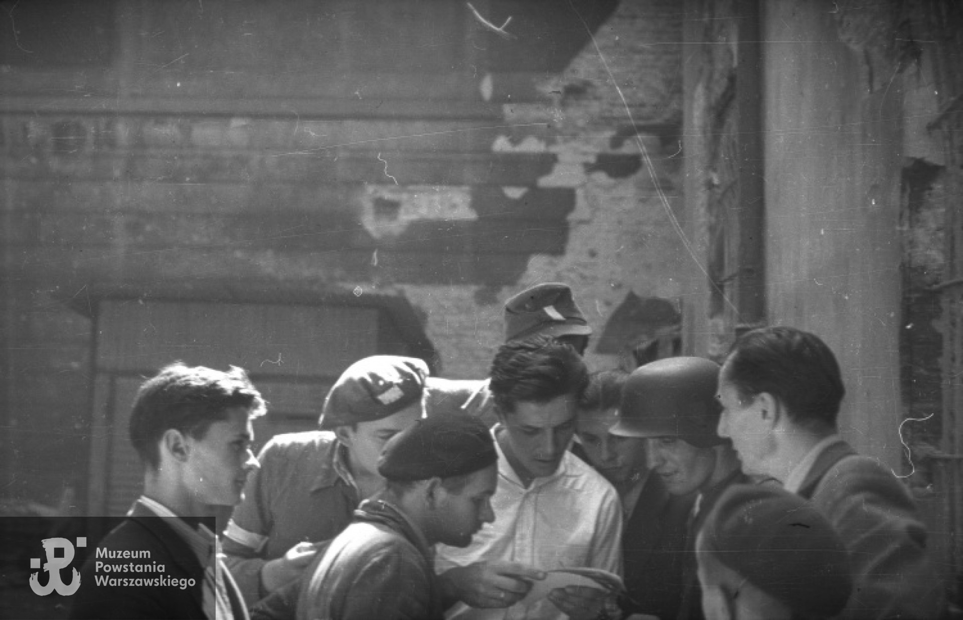 Grupa żołnierzy przeglądająca powstańcze fotografie. Po lewej, zwrócony profilem, fotograf Sylwester Braun  (pierwszy z prawej) Data wykonania: ok. 17 sierpnia 1944. Fot. Eugeniusz Haneman, zbiory MPW, sygn. MPW-IN/2963