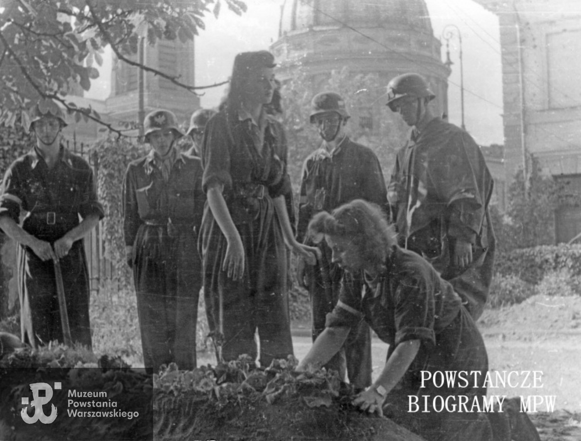 Fotografia z Powstania Warszawskiego. Pogrzeb strz. Witolda Hermanowskiego "Świta" z 1. plutonu "Kłosa" 3. kompanii "Redy" batalionu "Miłosz" na terenie Instytutu Głuchoniemych i Ociemniałych przy pl. Trzech Krzyży 2/3.Przy grobie "Świta" stoją: Juliusz Pietrzykowski "Teddy", Rola", łączniczka Hanna Baranowska "Lalka", "Peryskop", "Grom", klęczy "Aćka". Autorem zdjęcia jest Wojciech Marczyński "Bogusław". Ze zbiorów Muzeum Powstania Warszawskiego, sygn. MPW-IK/2374