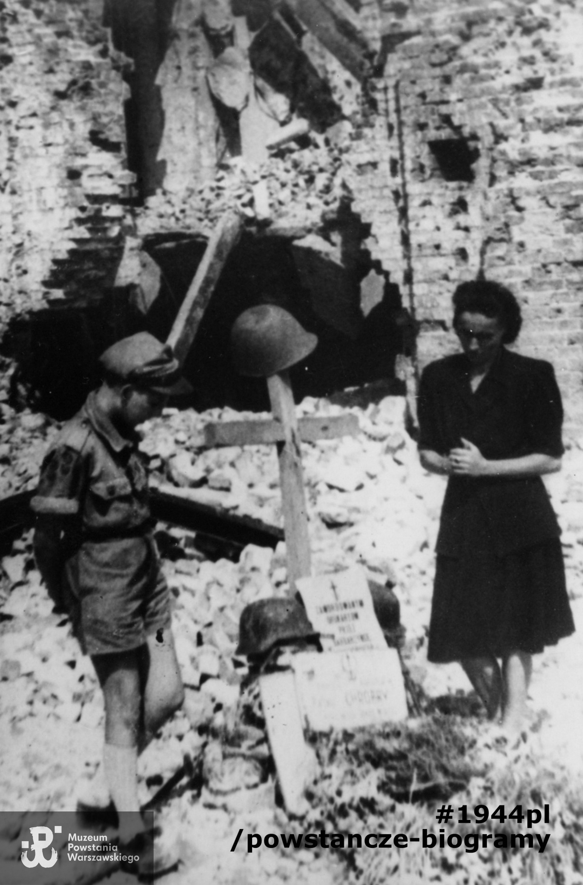 Fotografia powojenna, wykonana we wrześniu 1945 r. przedstawiającą p. Feliksę Paluchow, matkę poległego Henryka Paluchowa ps. Góral, przy krzyżu pamiątkowym przy ruinach pasażu Simonsa. Obok stoi harcerz, Jan Świderski. Przed krzyżem widoczne dwie tablice pamiątkowe,  "Pamięci Bohaterów Baonu Chrobry". Fotografię wykonał Zygmunt Sowiński "Ostoja". Zdjęcie pochodzi ze zbiorów prywatnych p. Andrzeja Michała Zielińskiego ps. Jędrek i zostało udostępnione do wykonania kopii przez p. Annę Witkowską. Ujęcie tożsame w zbiorach MPW: MPW-IP/7420 (P/7833/13), MPW-IP/7267.