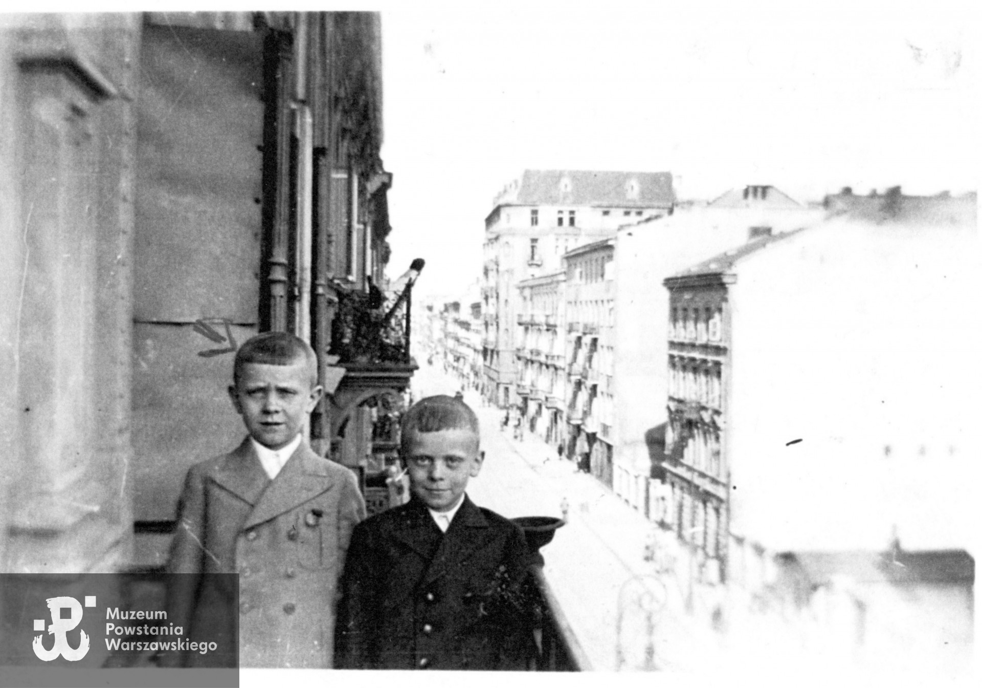 Tadeusz Różycki (na zdjęciu po lewej, w jasnej marynarce) na II piętrze kamienicy przy  ul. Złotej 54. Po prawej, w kierunku ul. Marszałkowskiej, 6-piętrowy dom przy nieistniejącej ulicy Sosnowej - przecznicy ul. Złotej. Wiosna 1943r. Fot. ze zbiorów Muzeum Powstania Warszawskiego, sygn. P/5779/07, dar p. Tadeusza Różyckiego ps. Dudek 
