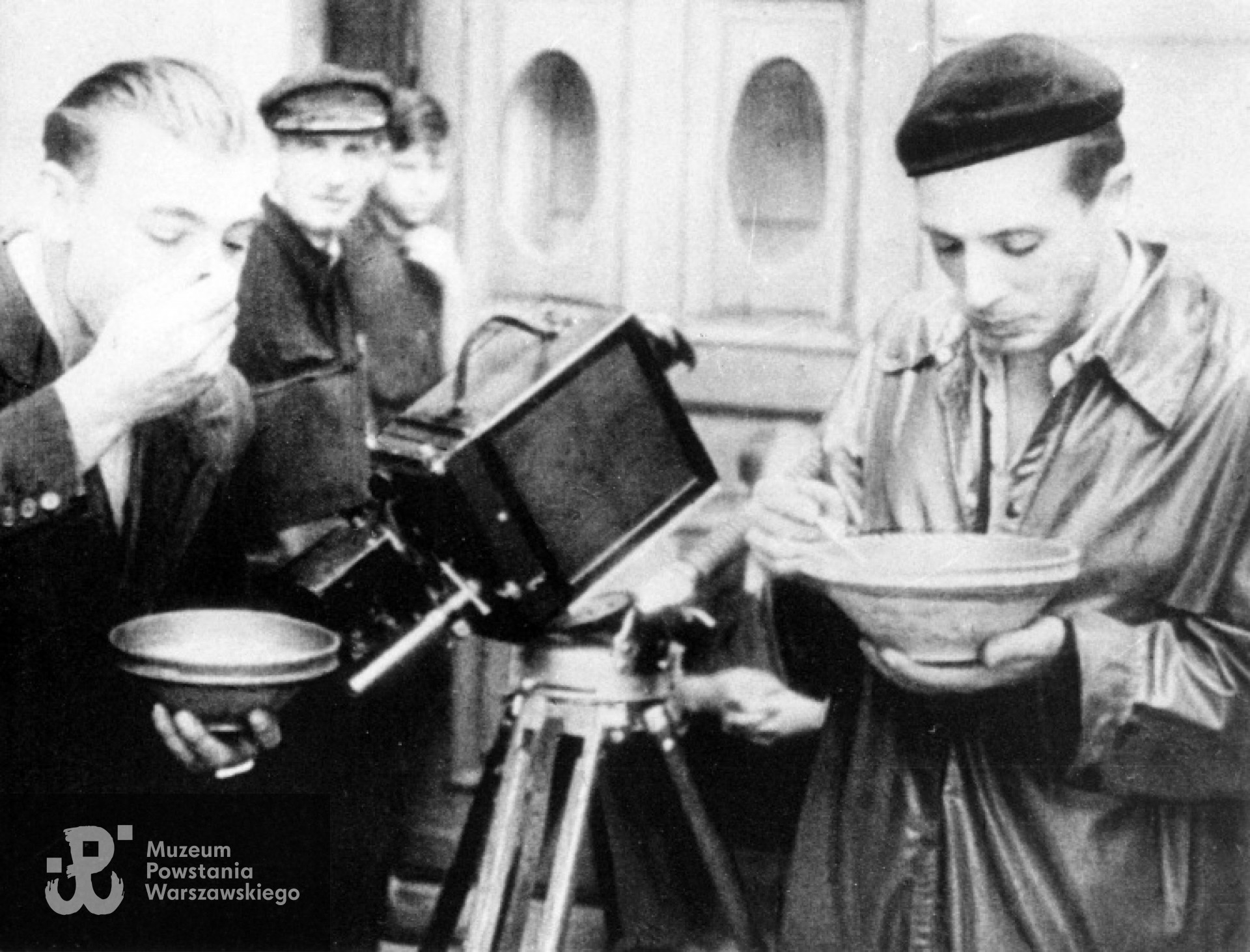 Śródmieście Północne - ul. Szpitalna.  Fotografia filmowa z Powstania Warszawskiego. Operator Ryszard Szope z bratem Edwardem podczas posiłku w kwaterze filmowców przy ul. Szpitalnej 8. W środku kamera "Ernemann". Autorem zdjęcia jest Henryk Vlassak. / zb.  MPW