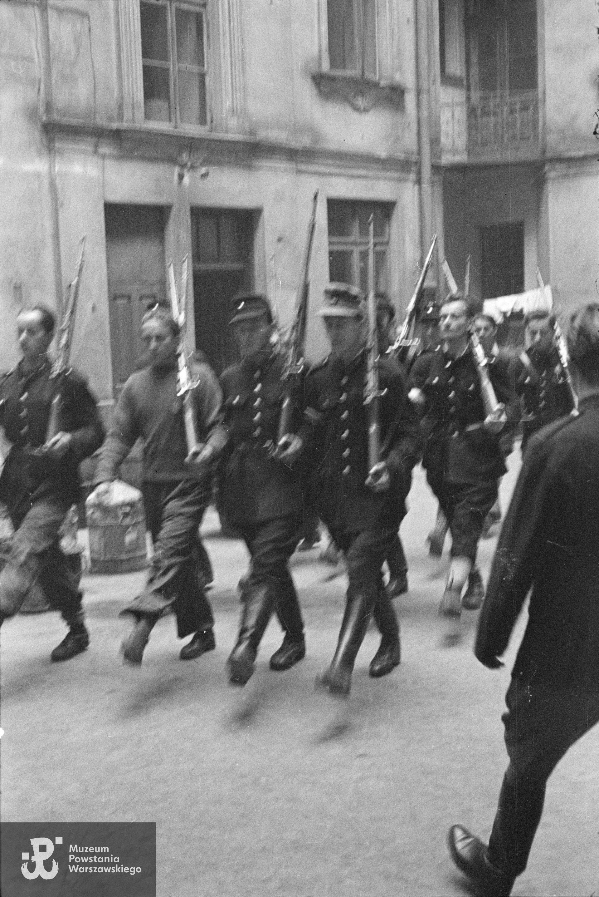  Fotografia z Powstania Warszawskiego. Śródmieście Północne. Musztra II plutonu kompanii "Koszta" na podwórzu kamienicy Jankowskiego przy ul. Moniuszki 12. W pierwszej czwórce od prawej: strz. Paweł Kowalczyk "Andrzej", st. strz. Tadeusz Jankowski "Owa", st. strz. Zdzisław Kamiński "Czarny", strz. Stanisław Zieliński "Zielony"; w drugiej czwórce: pierwszy od prawej st. strz. Henryk Gędziorowski "Henryk". Musztrę prowadzi plut. Edmund Klimaszewski "Jerzy" (wchodzi w kadr z prawej strony). Fot. ze zbiorów Muzeum Powstania Warszawskiego, sygn. MPW-IN/154