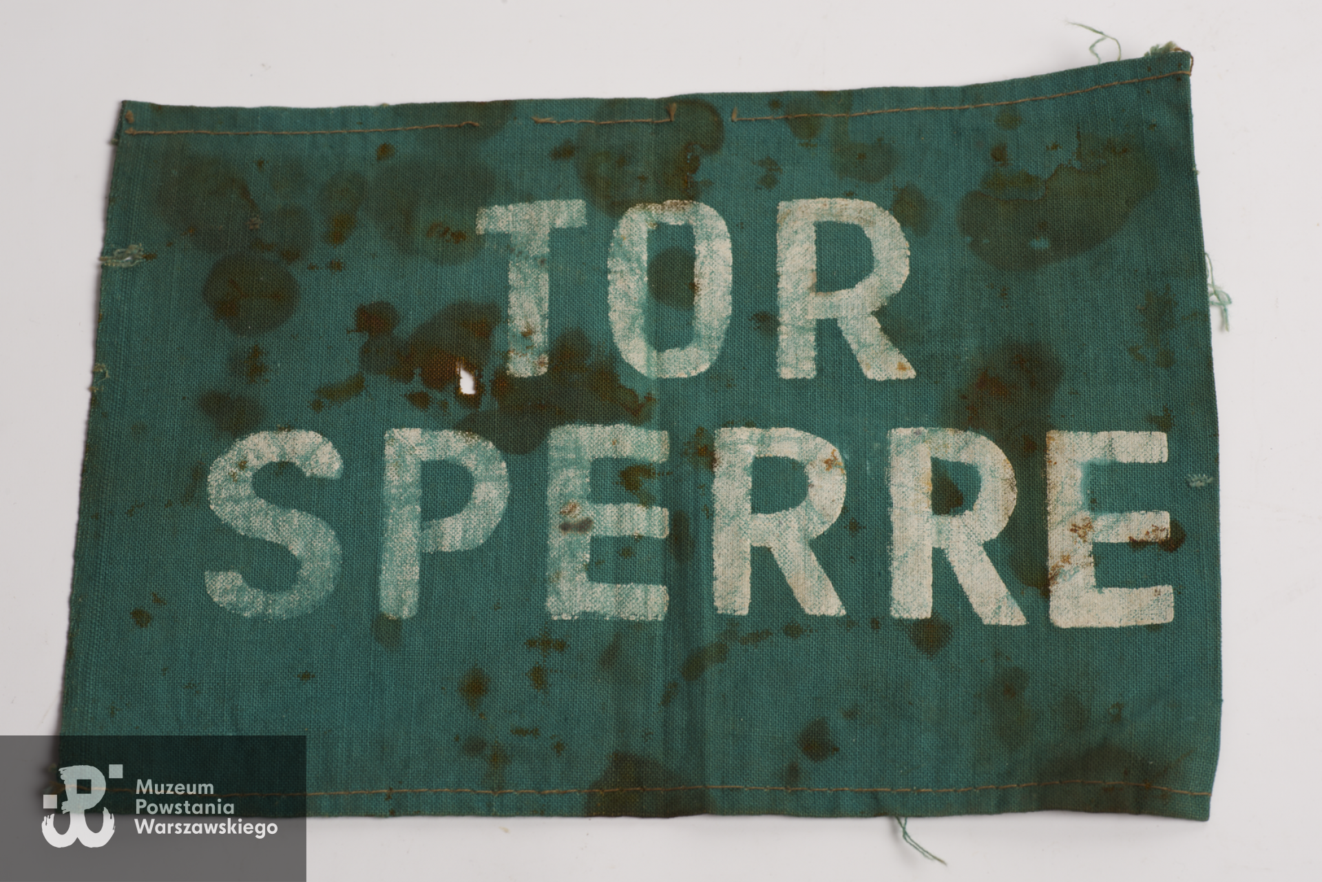 Opaska płócienna z napisem Tor sperre (brama zamknięta) noszona przez więźnia skazanego na karę śmierci, należąca do kpt. Władysława Klęka oficera Armii Krajowej skazanego na śmierć przez sąd wojskowy SS w niemieckim obozie jenieckim Sandbostel.  Zbiory Muzeum Wojska Polskiego w Sydney