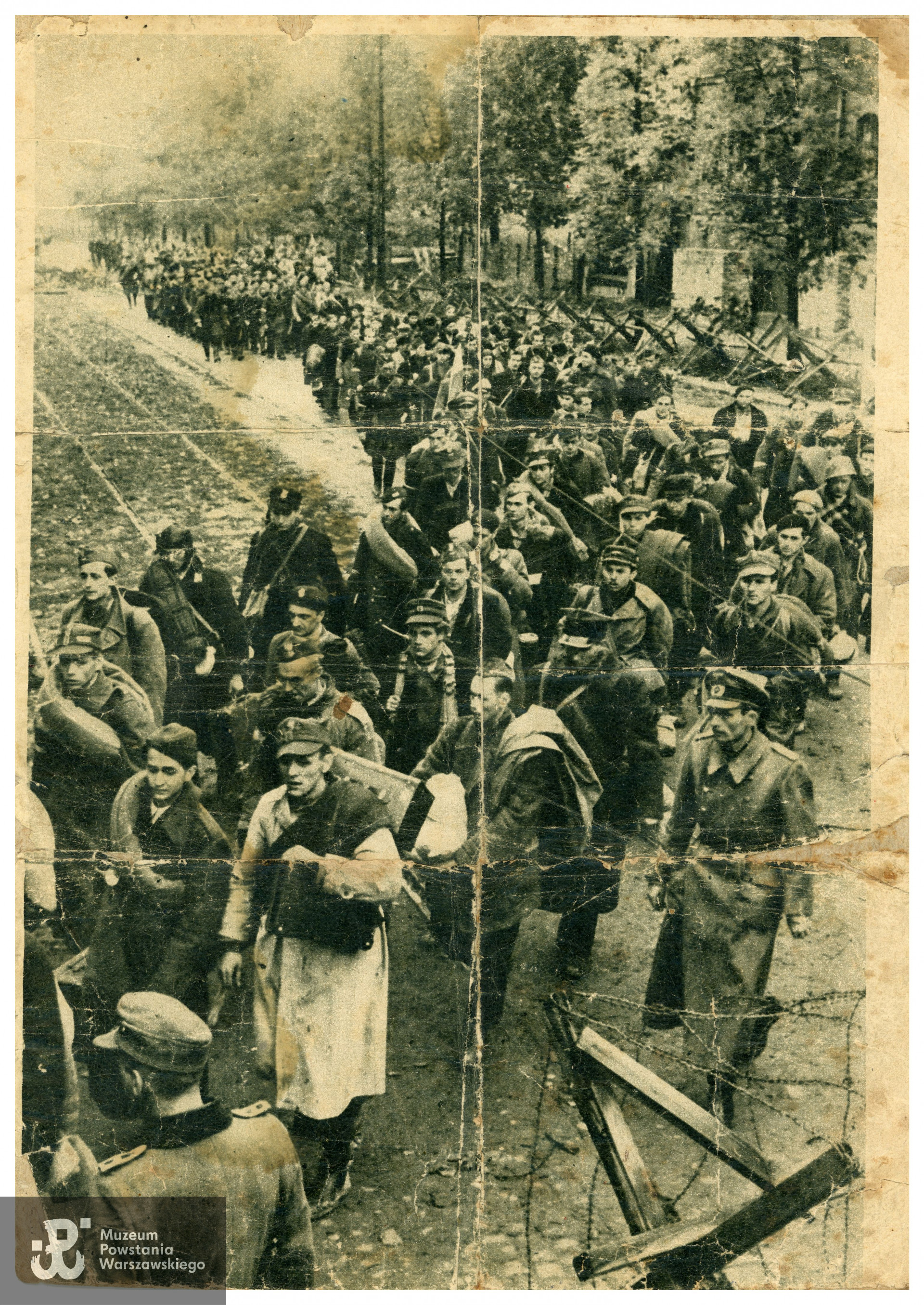 Zdjęcie przedstawiające wyjście Powstańców Warszawskich do niewoli. Według identyfikacji p. Mieczysława Ostanka, żołnierz obok powstańca w jasnym płaszczu to strz. Edmund Ostanek ps. „Gasparone”, „Sawicki". Według przekazu rodzinnego zdjęcie było urywkiem plakatu zerwanego ze słupa ogłoszeniowego po upadku Powstania Warszawskiego. Ze zbiorów p. Mieczysława Ostanka, syna Powstańca.