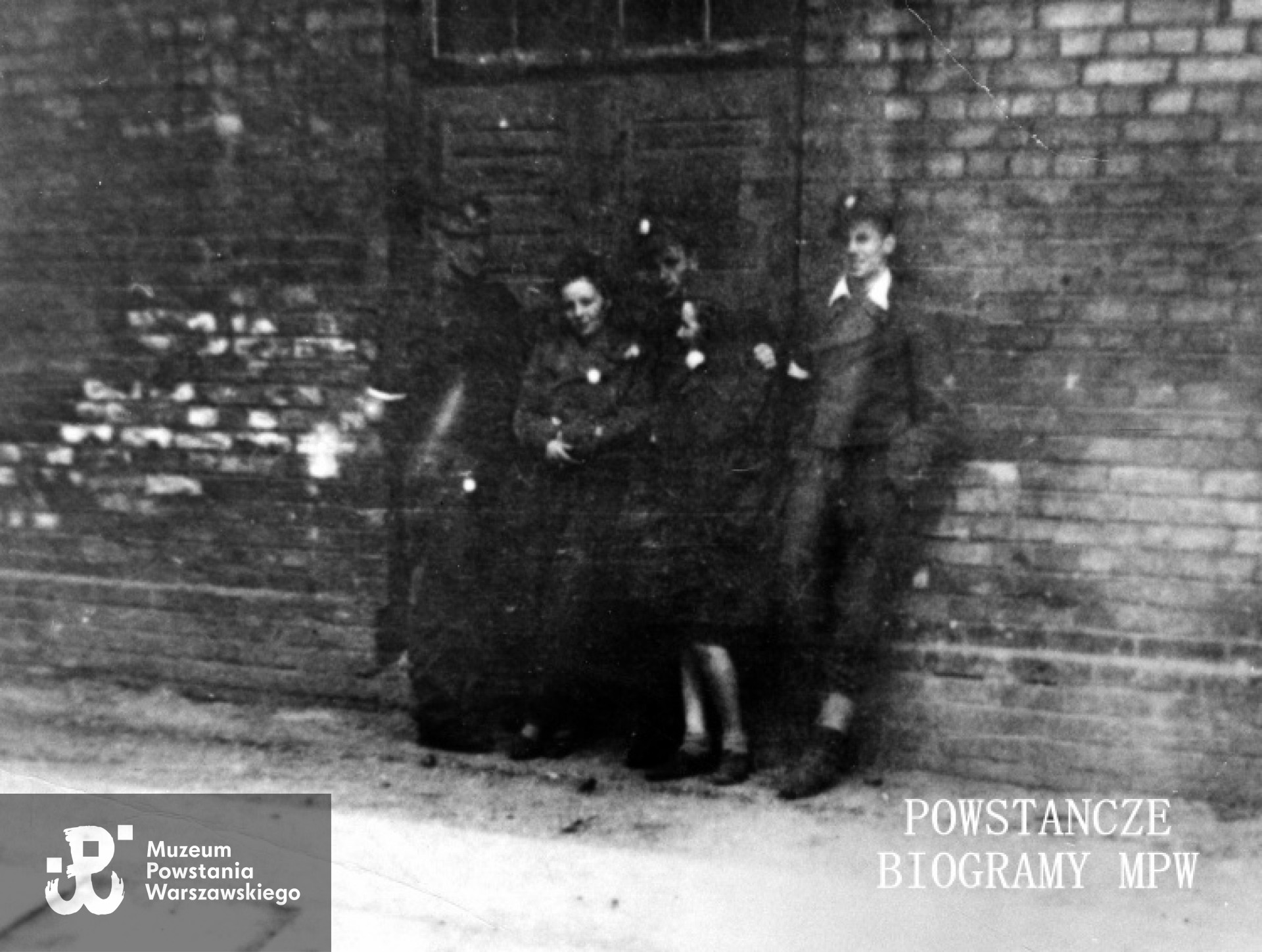 Fotografia z Powstania Warszawskiego. Stare Miasto, prawdopodobnie teren zakładów montażowych samochodów Fiata przy ul. Sapieżyńskiej. Grupa powstańców z Batalionu "Miotła" pluton "Torpedy", od lewej: ppor. Marian Ławacz "Marek", łączniczka Krystyna Trzaska "Krysia" (poległa 11 września 1944), plut. pchor. Janusz Gawdzik "Kruk" (poległ 25 sierpnia), Danuta Marciniak - Aniszewska "Danka", kpr. pchor. Zbigniew Wojterkowski "Bogdan". Fot. ze zbiorów Muzeum Powstania Warszawskiego, sygn. MPW-IK/1364