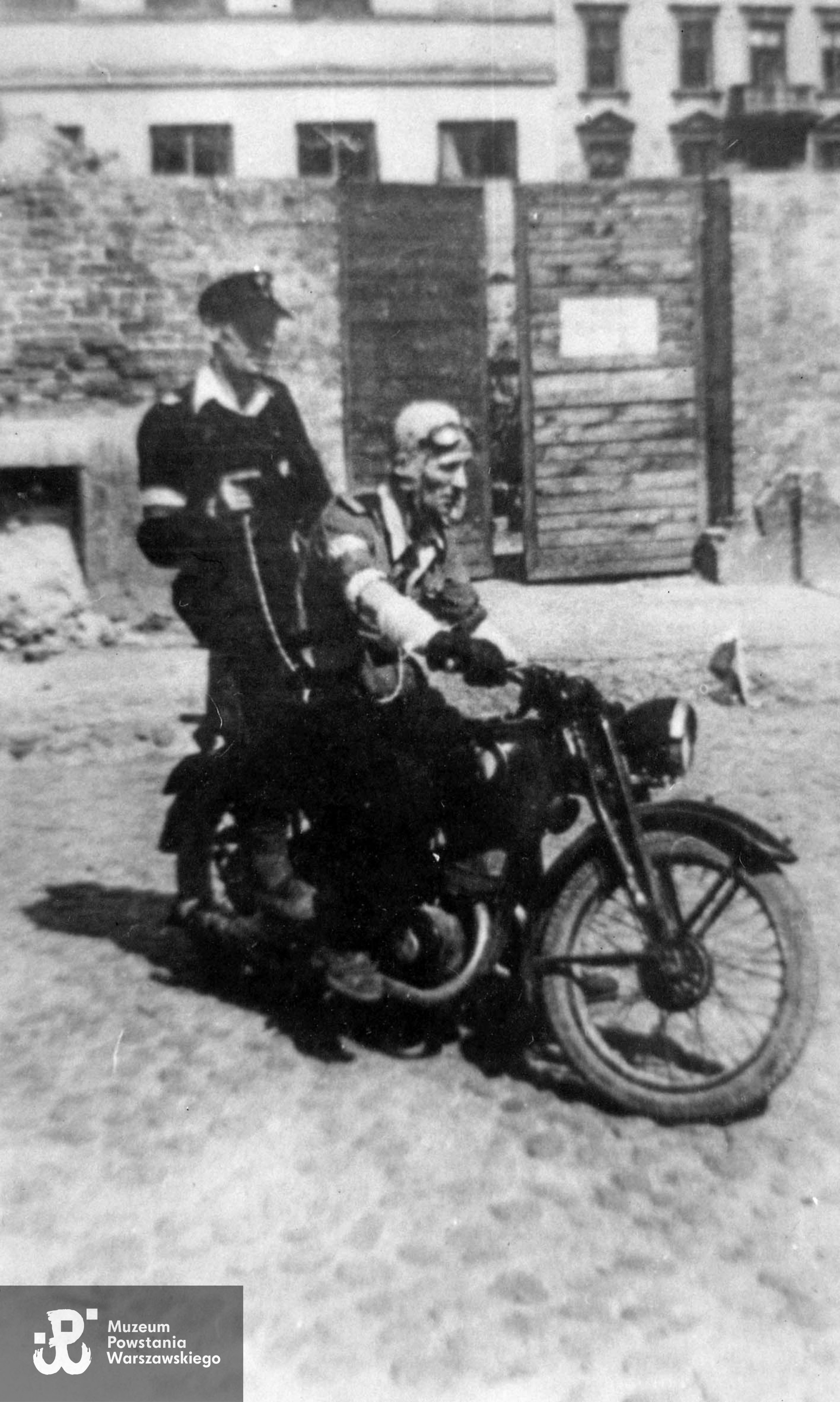 Fotografia z Powstania Warszawskiego. Śródmieście Północne. Drużyna motocyklistów z kompanii łączności Zgrupowania "Chrobry II" na ul. Siennej. Prowadzi plut. pchor. Kazimierz Szczeszek "Adam", z tyłu siedzi sierż. pchor. "Botanik". Za nimi widoczna brama wyburzonej posesji Sienna 52. Ujęcie w kierunku północnym. W tle po lewej dom Śliska 43, w prawym górnym rogu fragment kamienicy Śliska 44. Fot. ze zbiorów Muzeum Powstania Warszawskiego, sygn. MPW-IH/47