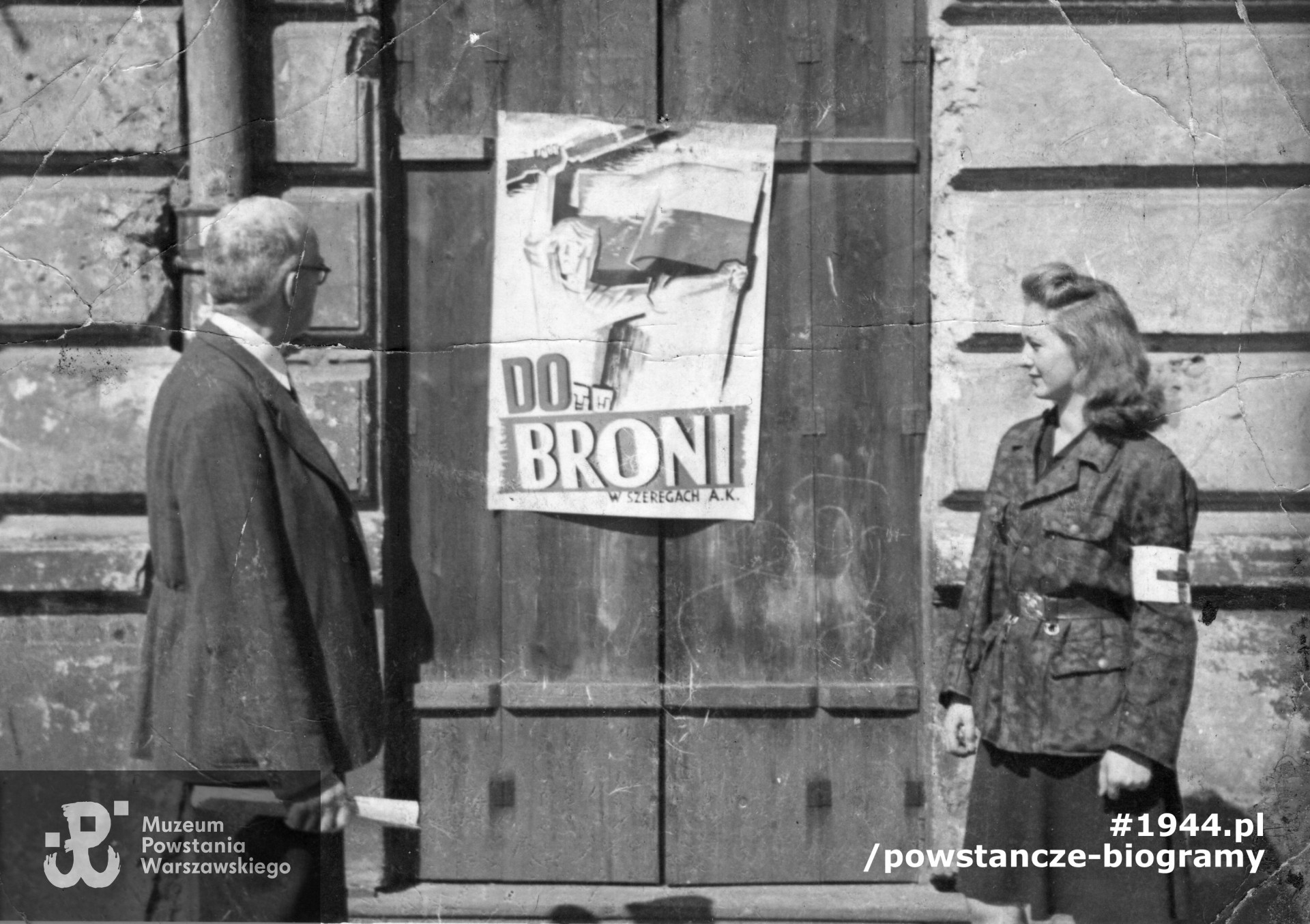 Fotografia z Powstania Warszawskiego. Janina Marisówna-Tomiak z ojcem, Adamem Tomiakiem, przed plakatem "Do broni!" przy ulicy Muranowskiej, Stare Miasto. Ze zbiorów Muzeum Powstania Warszawskiego, sygn. MPW-IP/4945/1