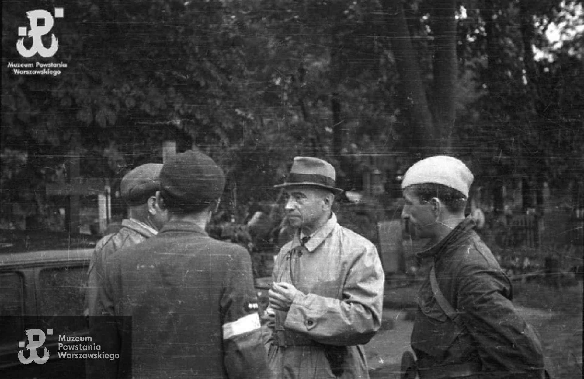 Wizytacja płka Kazimierza Iranka Osmeckiego "Makary" (w kapeluszu), szefa Oddziału II KG AK na cmentarzu ewngelicko-augsburskim. W rozmowie uczestniczą mjr Alfons Kotowski "Okoń" (po lewej) i por Stanisław Jankowskim "Agaton" (po prawej). Zdjęcie autorstwa Stefana Bałuka, ze zbiorów Fototeki MPW , sygnatura<a href=" http://www.1944.pl/galerie/fototeka/foto/7904/autor/126"> MPW-IS/130</a>