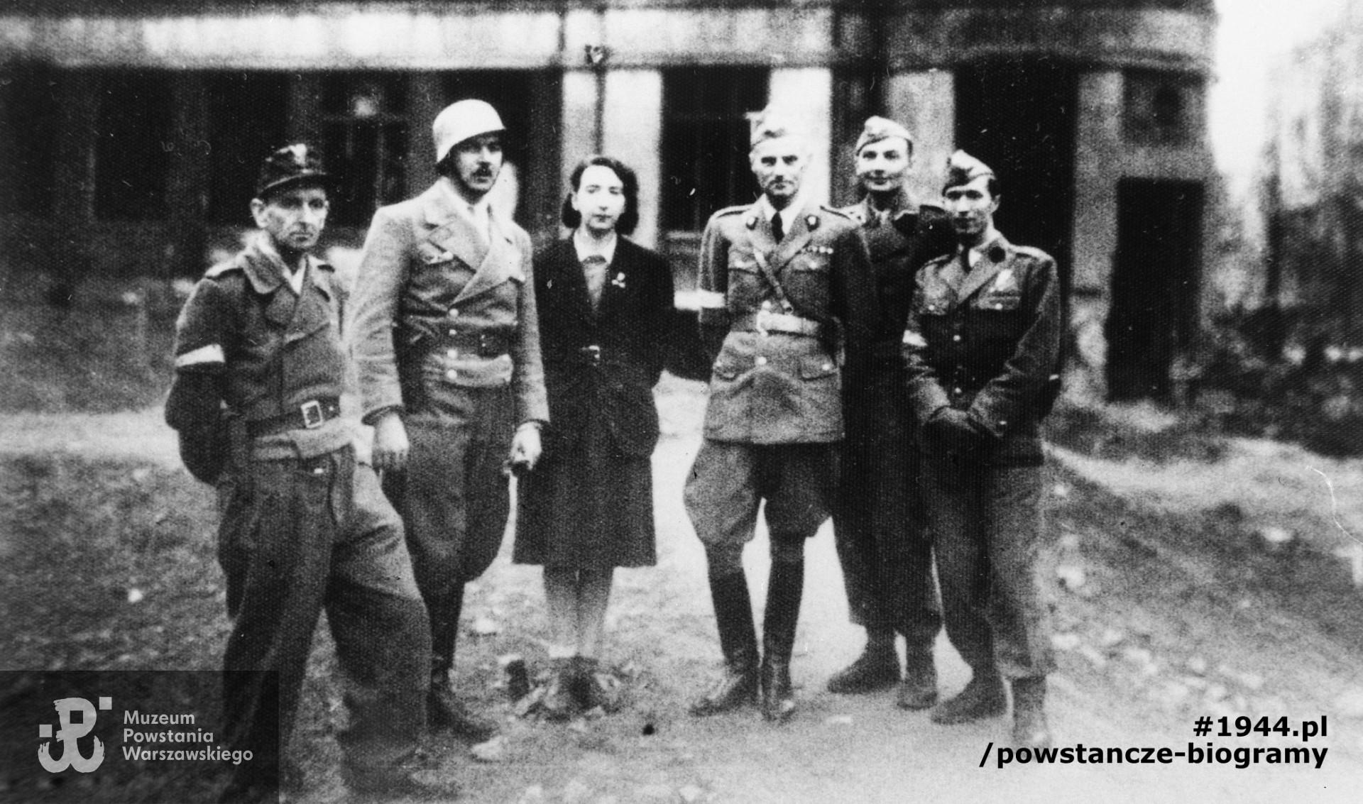 Fotografia z Powstania Warszawskiego. Śródmieście Północne. Grupa dowódców na placyku w rejonie zbiegu ulic Jasnej i Zgoda. Widoczni na zdjęciu: drugi od lewej major Włodzimierz Kozakiewicz „Barry”, obok łączniczka Irena Kwiatkowska „Basia”, pułkownik Karol Ziemski „Wachnowski” (dowódca grupy „Północ”), kapitan Eugeniusz Ihnatowicz-Suczyński „Kamiński”, kapitan Alfred Pokultinis „Fon”. W tle fragment elewacji Domu Pod Orłami. Fot. ze zbiorów Muzeum Powstania Warszawskiego, sygn. MPW-IH/4852