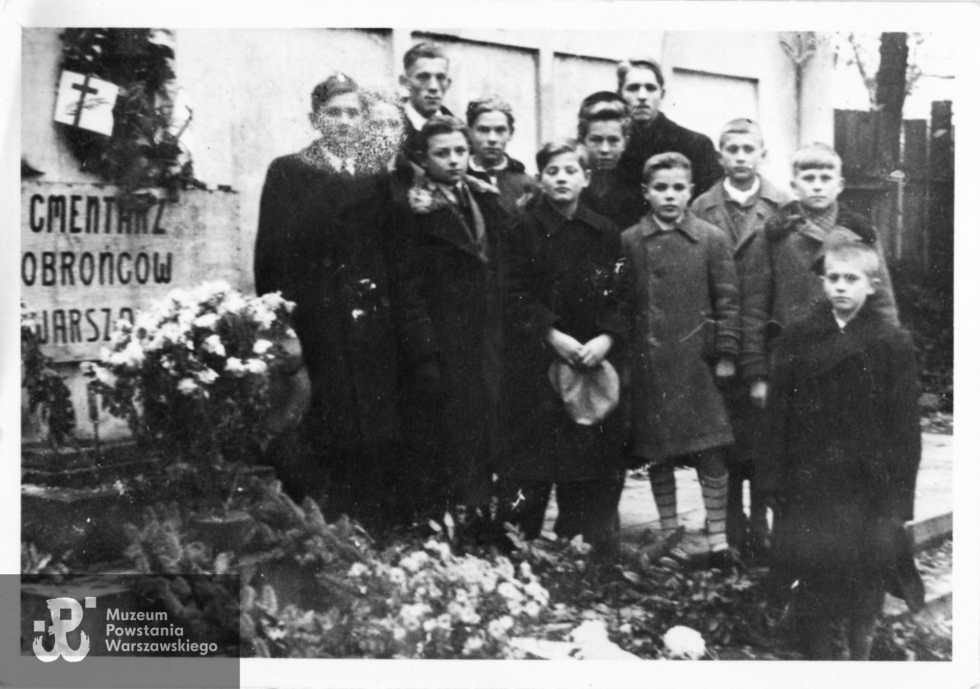 Cmentarz Obrońców Warszawy na terenie  Szpitala Ujazdowskiego. Fotografia wykonana  około 1940-1941 roku, przedstawiająca  grupę młodzieży, która w ramach działalności RGO brała udział w  koncertach organizowanych dla polskich żołnierzy rannych we wrześniu 1939 i leczonych w Szpitalu Ujazdowskim. Widoczni na zdjęciu od lewej: Czesław Parol, Jerzy Jóźwiak i Bogdan Parol, za nimi w II rzędzie 1) NN, 2) phm. Zbigniew Kamiński „Złoty Smok” (najwyższy), 3) Jerzy Dworak „Wesoły Tygrys", 4) Zofia (?) Krassowska i 5) Wołkowyski (imię nieustalone).  Pozostali chłopcy NN.  Ze zbiorów Muzeum Powstania Warszawskiego, sygn. P/6714