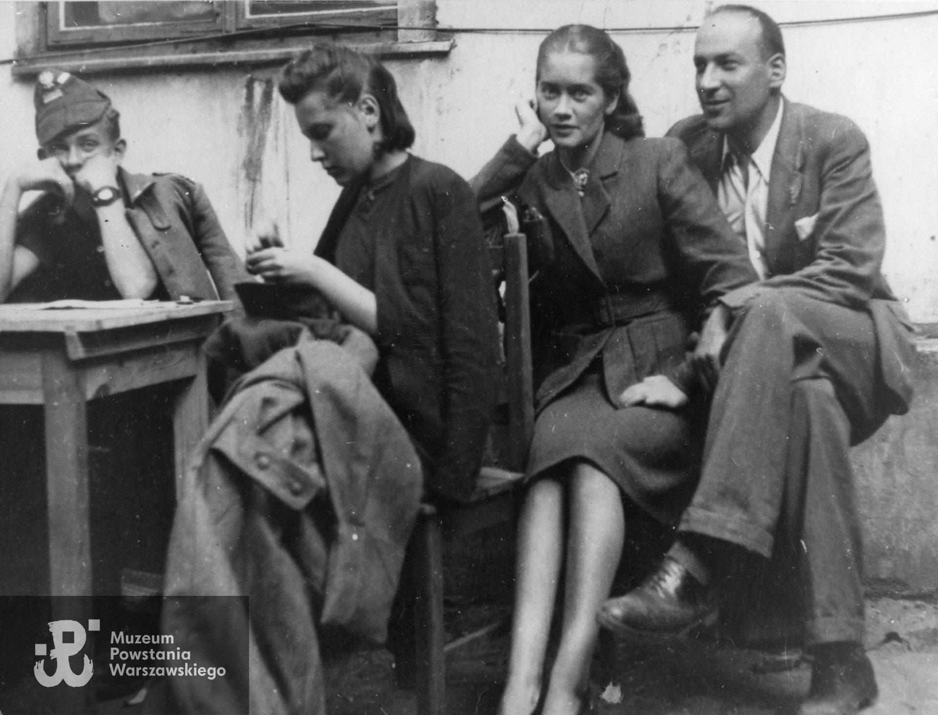 Fotografia z Powstania Warszawskiego. Śródmieście Północne, ulica Marszałkowska. Zaplecze kina "Stylowy". Przystosowywanie zdobycznych mundurów niemieckich. Od lewej: Andrzej Smoleński "Andrzej"; NN; Alina Janowska "Alina" oraz Włodzimierz Horbaczewski "Węgliński". Autor zdjęcia nieznany - prawdopodobnie Antoni Czermiński "Anton". Ze zbiorów Muzeum Powstania Warszawskiego, sygn. MPW-IK/2153