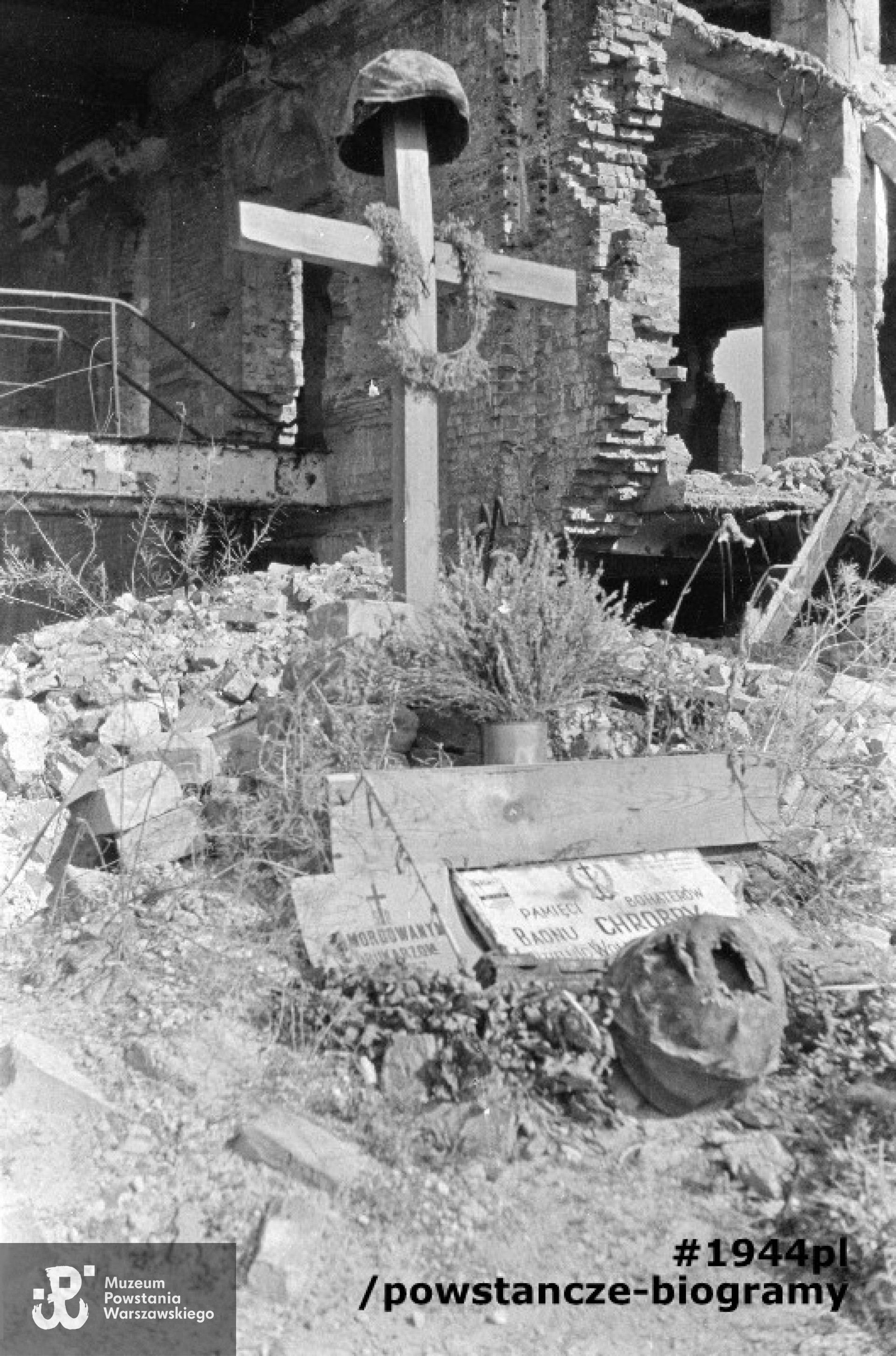 Fotografia powojenna. Krzyż pamiątkowy przy ruinach pasażu Simonsa przy ul. Bohaterów Getta (dawna Nalewki, ob. Stare Nalewki). Na krzyżu zawieszony wieniec i hełm. Przed krzyżem dwie tablice pamiątkowe: "Pamięci Bohaterów Baonu Chrobry [...] dzielnic Wola [...]" oraz "Pomordowanym drukarzom". Przy tablicach przerdzewiały hełm. Autorem zdjęcia jest Tadeusz Bukowski ,,Bończa". Zbiory Muzeum Powstania Warszawskiego, sygn.  MPW-IN/12516