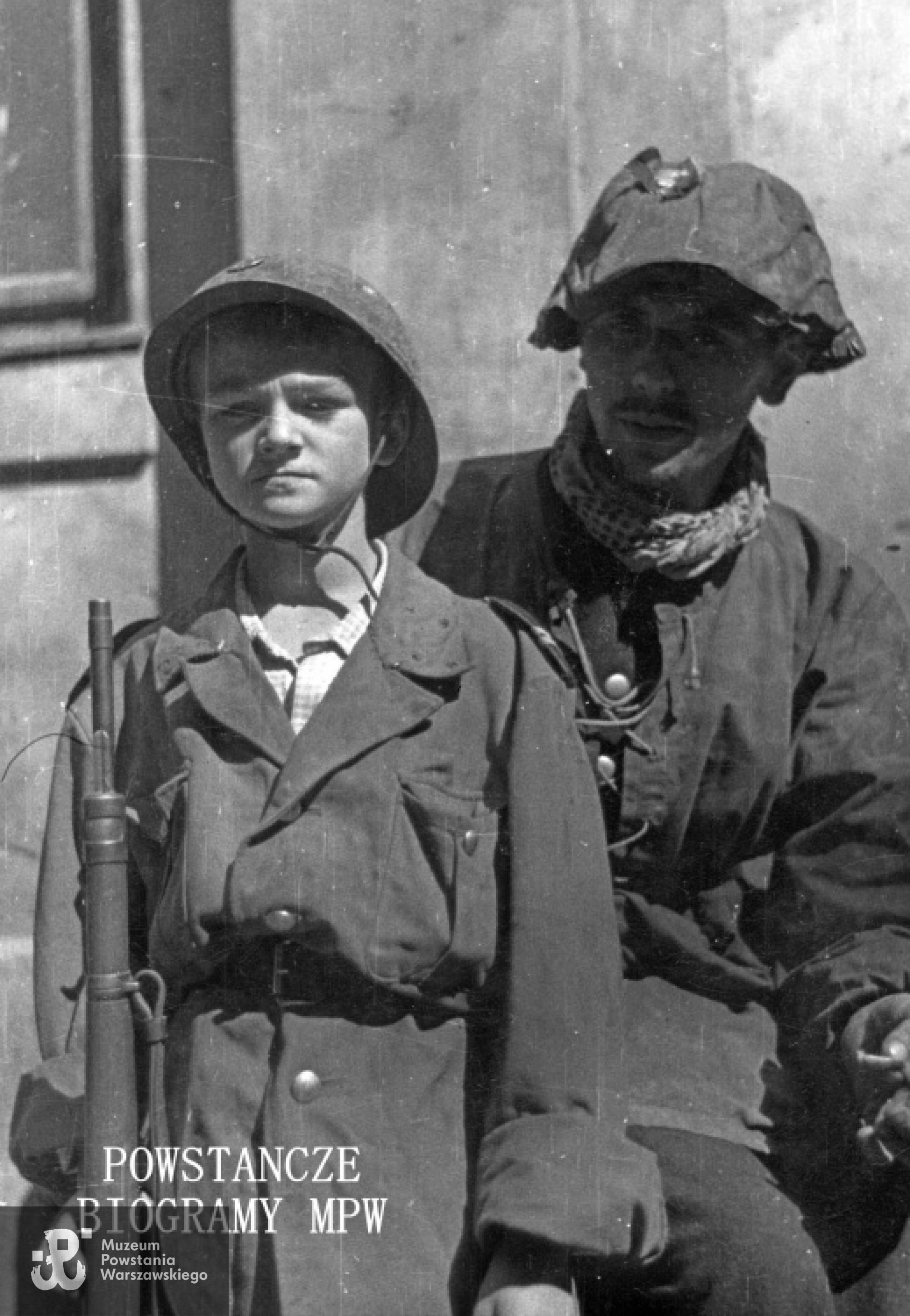 Fotografia z Powstania Warszawskiego. Śródmieście Północ. Powstańcy z Batalionu "Parasol" po ewakuacji ze Starówki na podwórzu domu Wedla przy ul. Szpitalnej 8. Po lewej stoi 12-letni kpr. Witold Modelski "Warszawiak", po prawej strz. Wiesław Kalinowski "Arab". Ze zbiorów Muzeum Powstania Warszawskiego, sygn. MPW-IK/2776