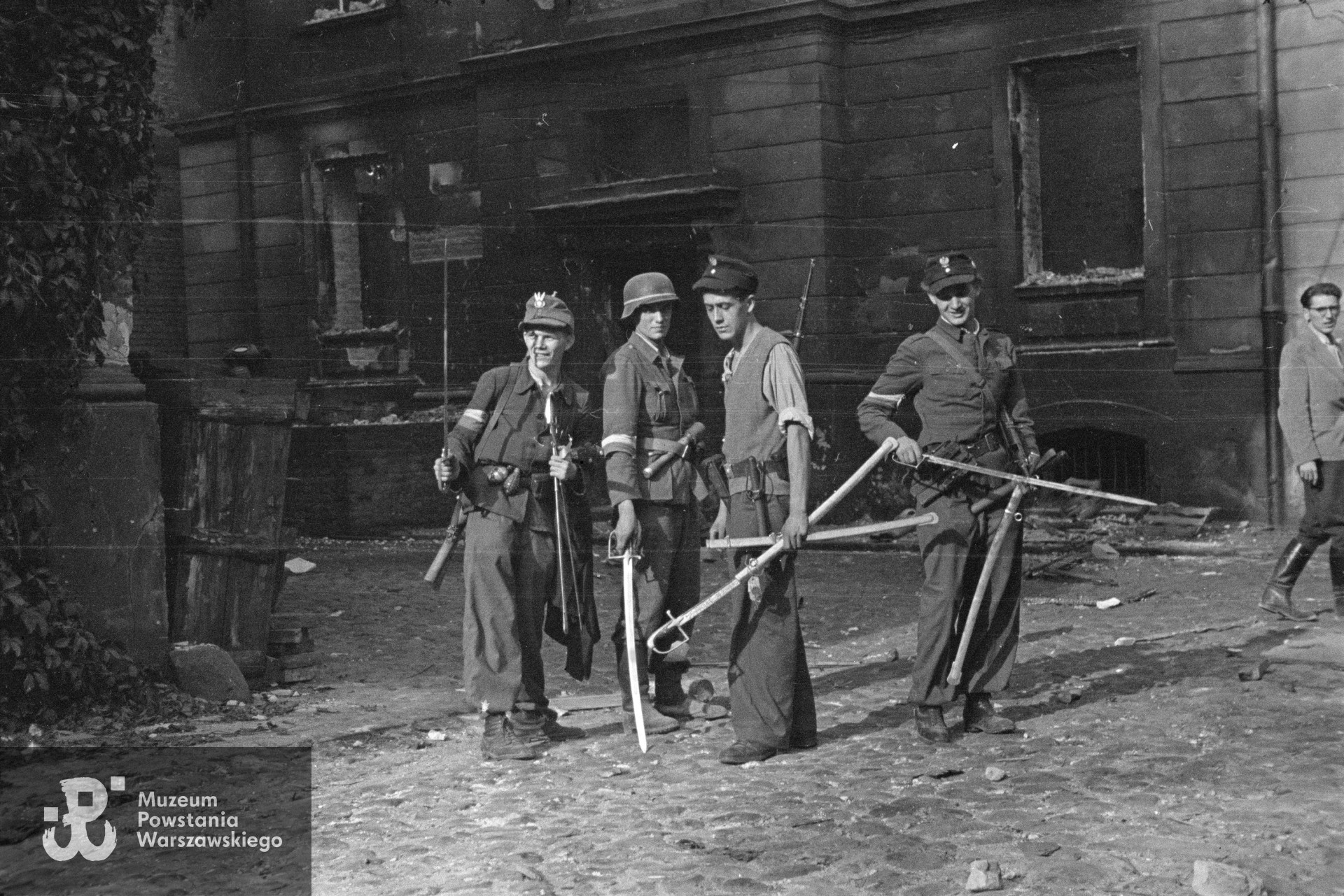 Fotografia z Powstania Warszawskiego. Śródmieście Północne. Grupa Powstańców z kompanii "Koszta" z szablami na dziedzińcu zdobytego gmachu Komendy Policji przy Krakowskim Przedmieściu 1. Drugi od lewej stoi plut. pchor. Jerzy Tyczyński "Jur" z niemieckim granatem trzonkowym wz. 1924 za pasem. Fot. autorstwa Eugeniusza Lokajskiego ps. "Brok". Ze zbiorów Muzeum Powstania Warszawskiego, sygn. MPW-IN/756.