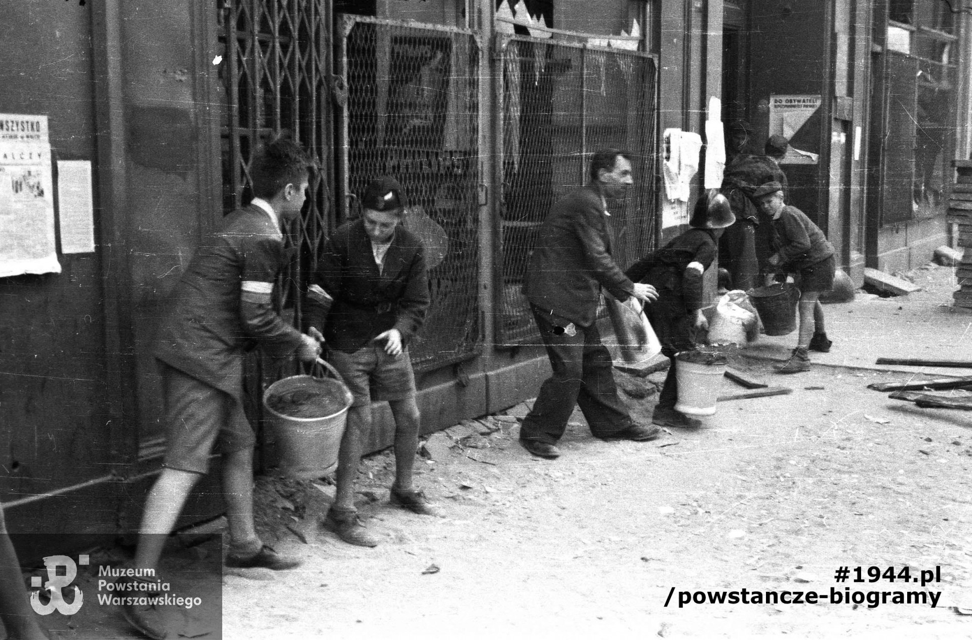 Fotografia z Powstania Warszawskiego. Śródmieście Północne. Grupa harcerzy pomagająca w akcji tłumienia pożaru kamienicy przy ul. Zgoda 15. Drugi od lewej Wojciech Ciążyński "Malec", w hełmie strażackim łącznik Zbigniew Ślęzakowski "Kędziorek". Autorem zdjęcia jest Eugeniusz Lokajski ps. Brok. Ze zbiorów Muzeum Powstania Warszawskiego, sygn. MPW-IN/441