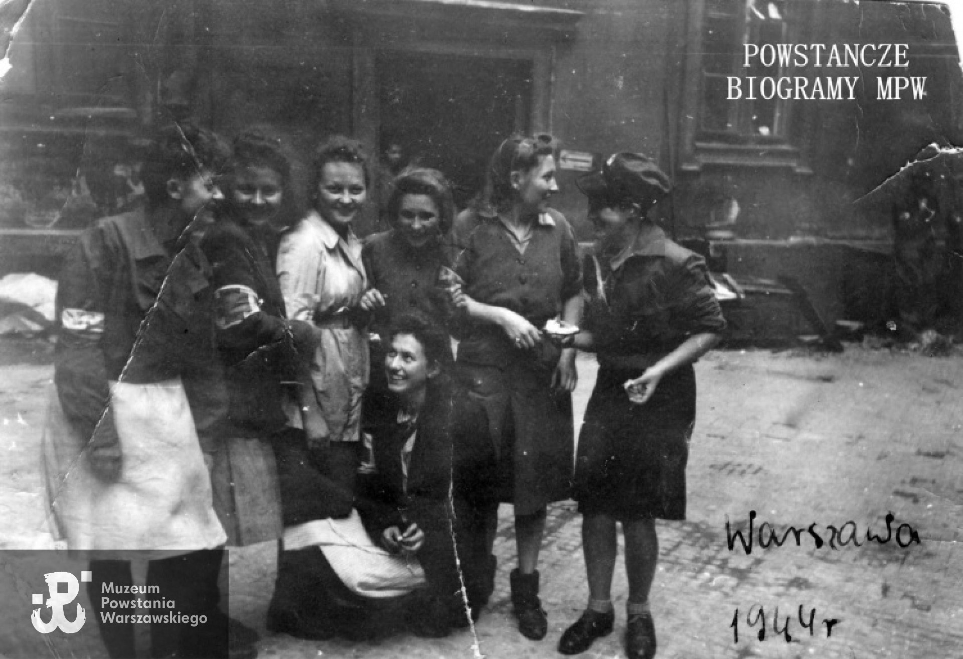 Fotografia z Powstania Warszawskiego autorstwa Joachima Joachimczyka ps. "Joachim".  Śródmieście Północne. Grupa sanitariuszek i łączniczek z plutonu 569 -  2. Harcerskiej Baterii Artylerii Przeciwlotniczej "Żbik" na podwórzu kamienicy Chmielna 57. Na zdjęciu od lewej: NN, sanit. Krystyna Kamać "Szafrańska", sanit. Jadwiga Mundkowska "Dina Pękałówna",  łączn. Irena Loga "Modrzewska", łączn. Halina Loga "Średzka", łączn. Maria Sturgólewska "Poręba",sanit. Stanisława Gawlik "Stenia". Ze zbiorów Muzeum Powstania Warszawskiego, sygn. MPW-IP/2109