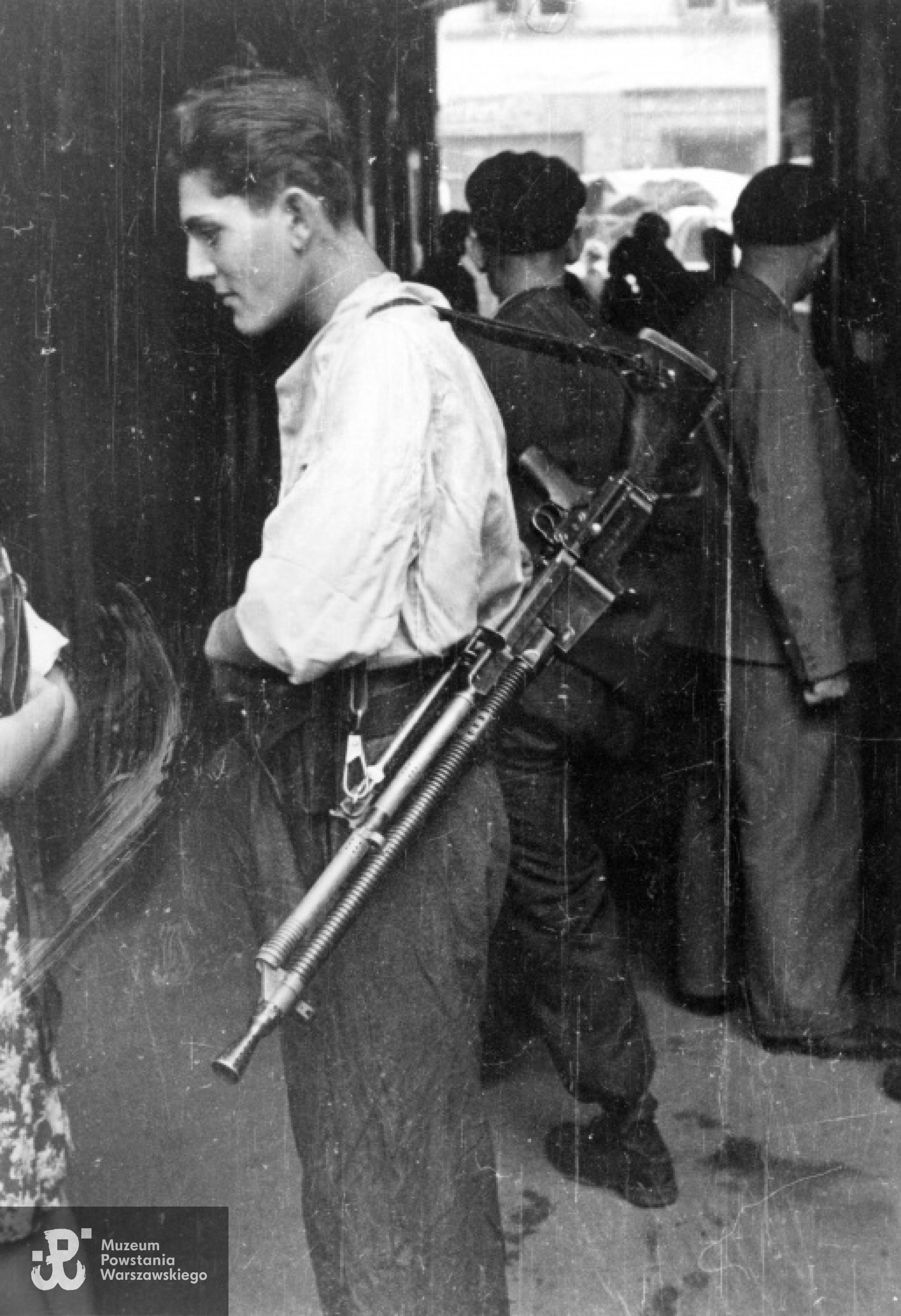 Plut. pchor. Włodzimierz Wiśniewski "Cygan" z kompanii "Janusza" z Batalionu "Harnaś" stojący w bramie kamienicy z ręcznym karabinem maszynowym Cz Zbrojovka wz. 26 ze zrzutu. Fotografia  autorstwa Eugeniusza Lokajskiego, prawa autorskie: MPW. Zbiory Fototeki MPW, sygn. MPW-IN/732