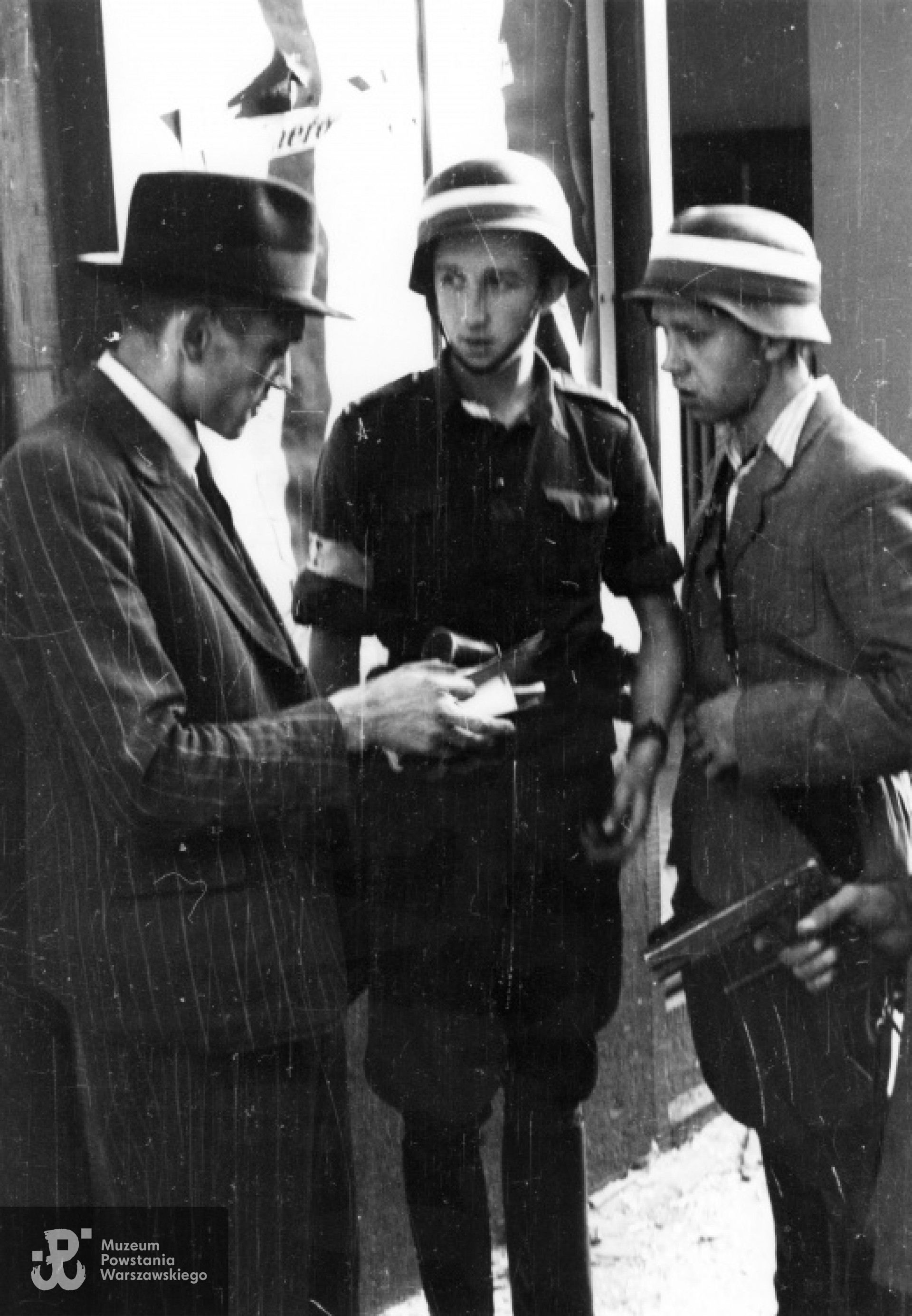 Fotografia z Powstania Warszawskiego. Dwóch powstańców z kompanii "Koszta" legitymuje cywila; od lewej: kpr. Andrzej Główczewski "Marek" i st. strz. Wacław Krupiński "Belina". Fot. Eugeniusz Lokajski "Brok". Zbiory fototeki MPW, sygn. MPW-IN/28; prawa autorskie: MPW