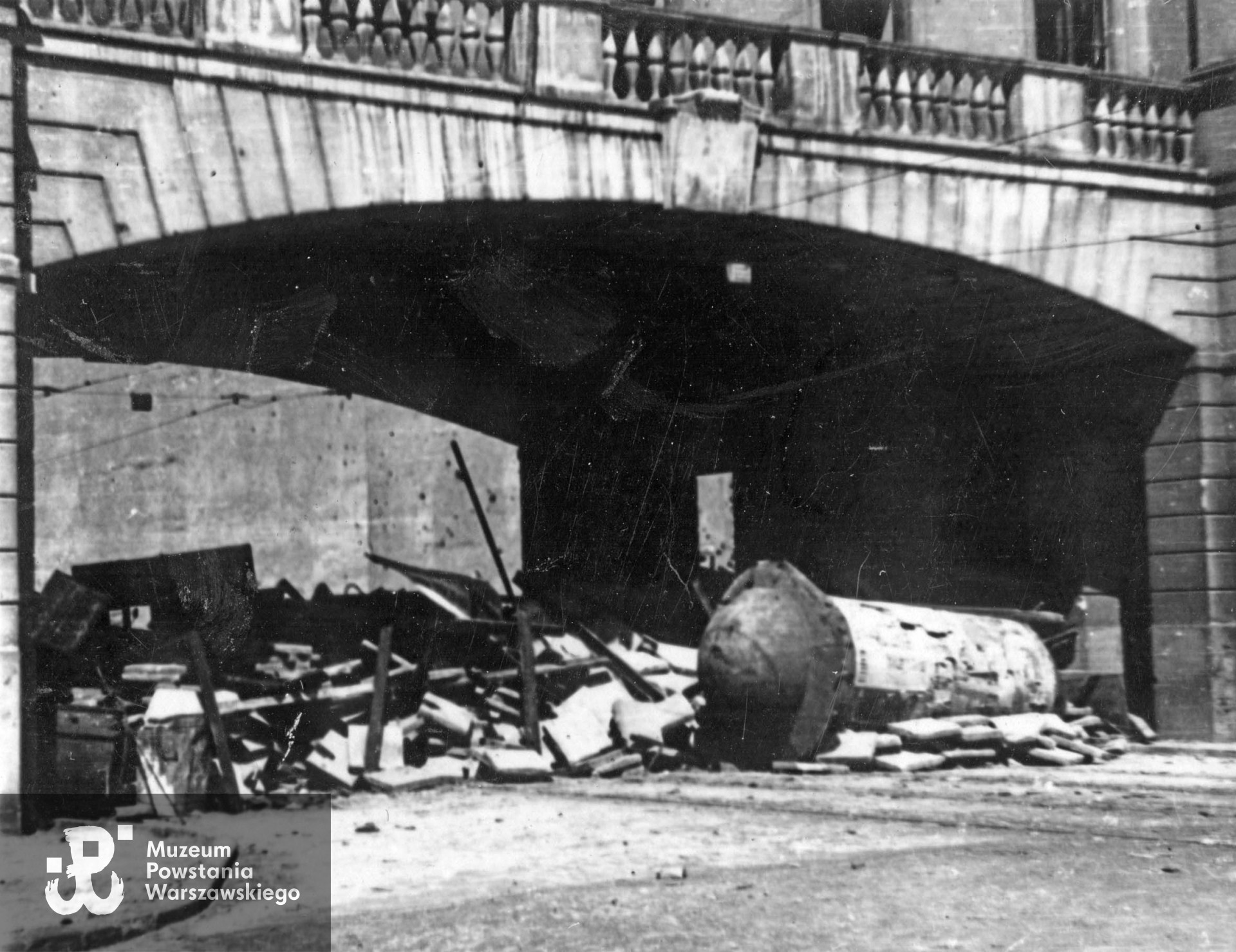 Fotografia autorstwa Zbigniewa Grochowskiego wykonana podczas Powstania Warszawskiego. Barykada w przejeździe pod budynkiem Sądu Okręgowego - plac Krasińskich 12. W tle widoczna ślepa ściana kamienicy przy ul. Świętojerskiej 22, róg Nowiniarskiej 7. Fot. ze zbiorów Muzeum Powstania Warszawskiego, sygn. MPW-IP/2712 (MPW-GI-4000/15/06)