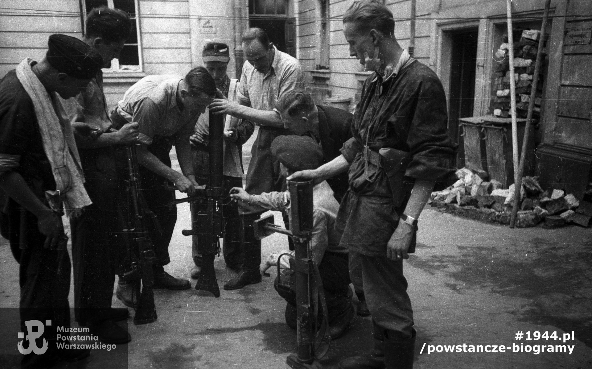 Plut. pchor. Adam Podkóliński "Michał", "Olszewski" (trzeci od lewej) prezentuje grupie powstańców z kompanii "Janusza" z batalionu "Harnaś" niemiecki lekki karabin maszynowy (leMG 08/15) zdobyty po ataku na Komendę Policji. Powstaniec na pierwszym planie po prawej trzyma brytyjski granatnik przeciwpancerny PIAT. Fot. ze zbiorów Muzeum Powstania Warszawskiego, sygn. MPW-IN/10204. Autorem zdjęcia jest Joachim Joachimczyk "Joachim"