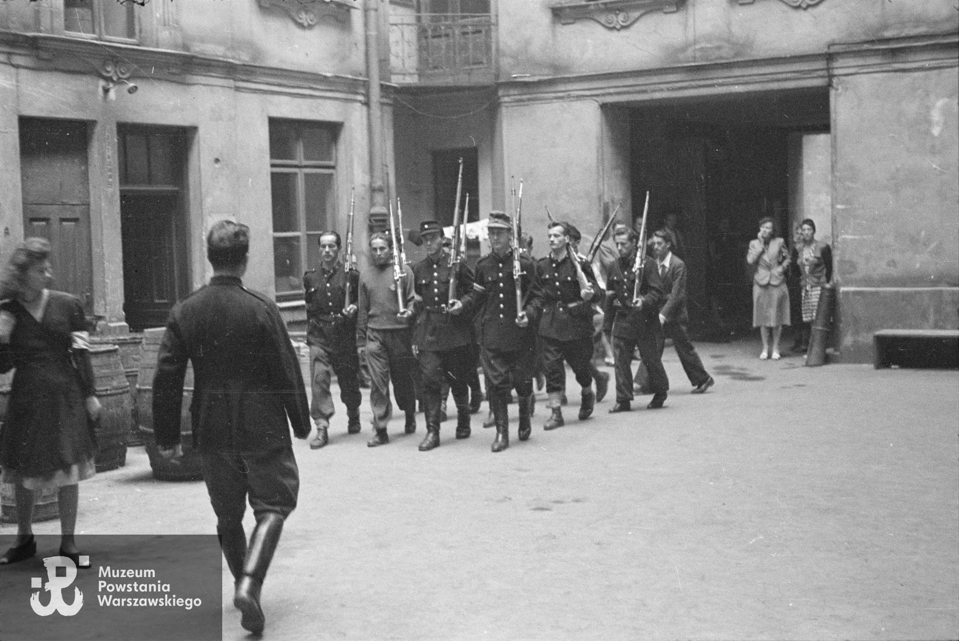  Śródmieście Północne. Musztra II plutonu kompanii "Koszta" na podwórzu kamienicy Jankowskiego przy ul. Moniuszki 12. W pierwszej czwórce od prawej: strz. Paweł Kowalczyk "Andrzej", st. strz. Tadeusz Jankowski "Owa", st. strz. Zdzisław Kamiński "Czarny", strz. Stanisław Zieliński "Zielony"; w drugiej czwórce: pierwszy od prawej st. strz. Henryk Gędziorowski "Henryk"; musztrę prowadzi plut. Edmund Klimaszewski "Jerzy". Fot. ze zbiorów Muzeum Powstania Warszawskiego, sygn. MPW-IN/155