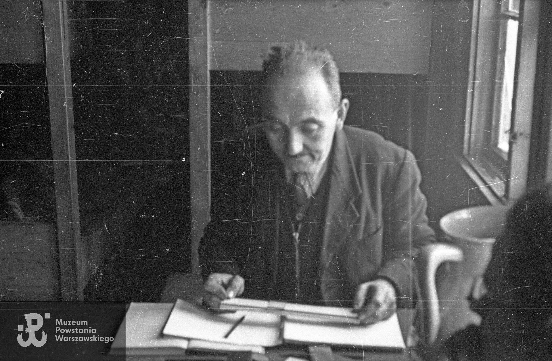 Fotografia ze Stalagu XI B/z w Bergen-Belsen autorstwa Wiesława Chrzanowskiego ps. "Wiesław". Wnętrze baraku nr 198.  Ppor. Jarosław Naleszkiewicz z Delegatury Rządu na Kraj z przyborami matematycznymi przy stole. Fot. ze zbiorów Muzeum Powstania Warszawskiego, sygn. MPW-IN/3385