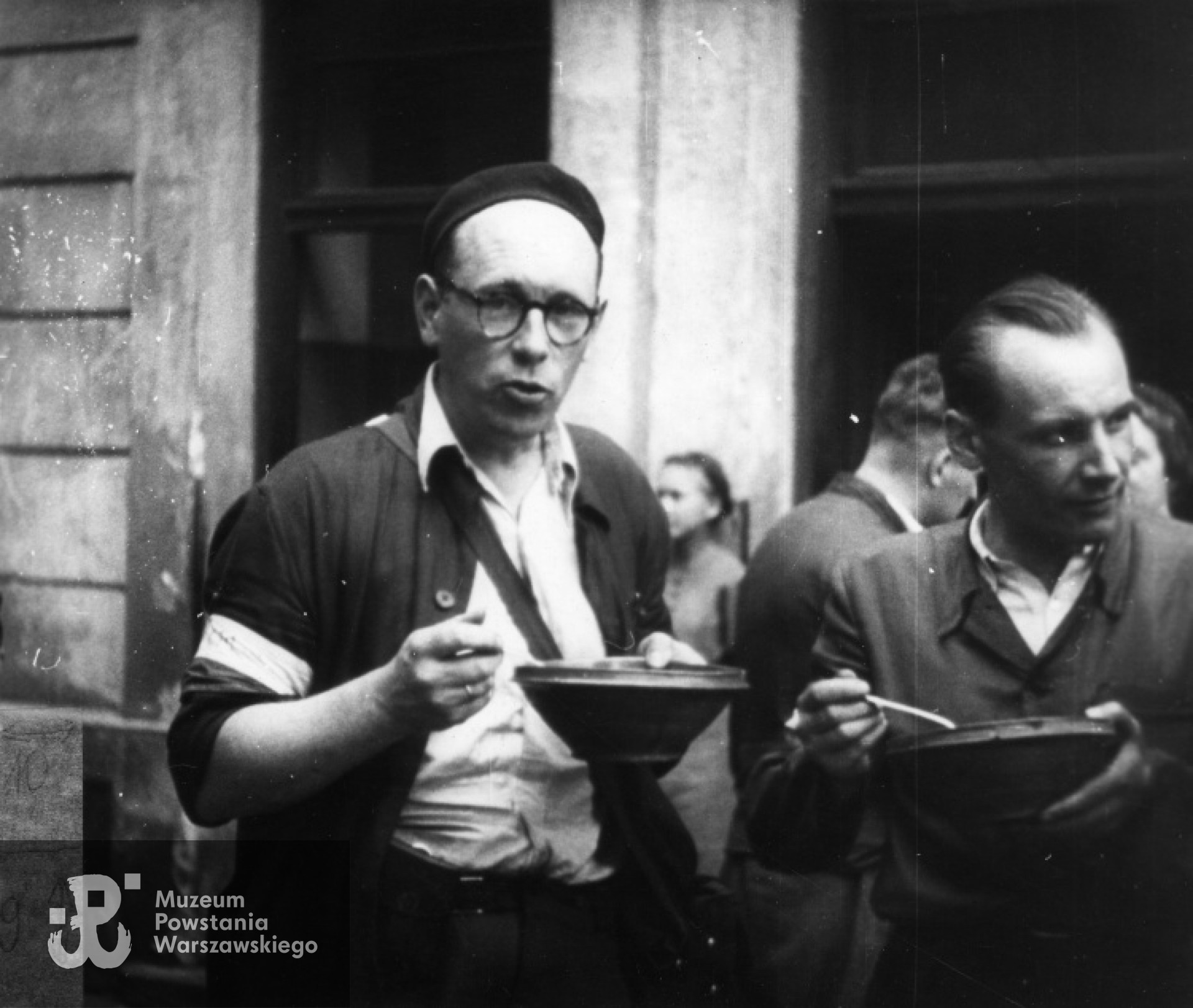 Śródmieście Północne. Powstańcza stołówka przy ul. Szpitalnej 8. Operator Henryk Vlassak (po lewej) podczas spożywania posiłku, prawdopodobnie sierpień 1944 r. Ze zbiorów Muzeum Powstania warszawskiego.