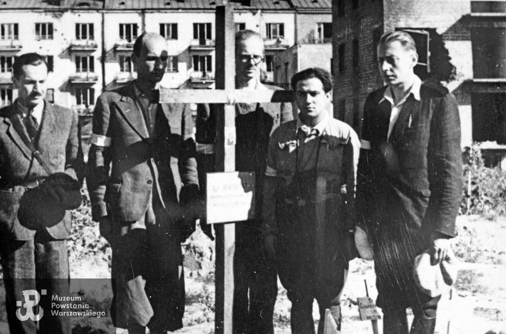 Zdjęcie filmowe z Powstania Warszawskiego. Mokotów, cmentarz powstańczy przy Szpitalu Elżbietanek w rogu ulic Goszczyńskiego i Tynieckiej. W tle budynki Odyńca 11-13. Grupa powstańców z Grupy Artyleryjskiej "Granat" przy grobie dowódcy, mjr art. Józef Szyszko "Bachmat", który zginął 13 sierpnia. Stoją od lewej: ppor. Stanisław Saryusz-Wolski "Szrapnel", kpr. pchor. Zbigniew Grochowski "Roma" "Mazur" (?), por. Adam Jastrzębski "Różan", ppor. Waldemar Olszewski "Waldemar", ppor. Stanisław Kietliński "Hel". Ze zbiorów Muzeum Powstania Warszawskiego, sygn. MPW-IH/1215