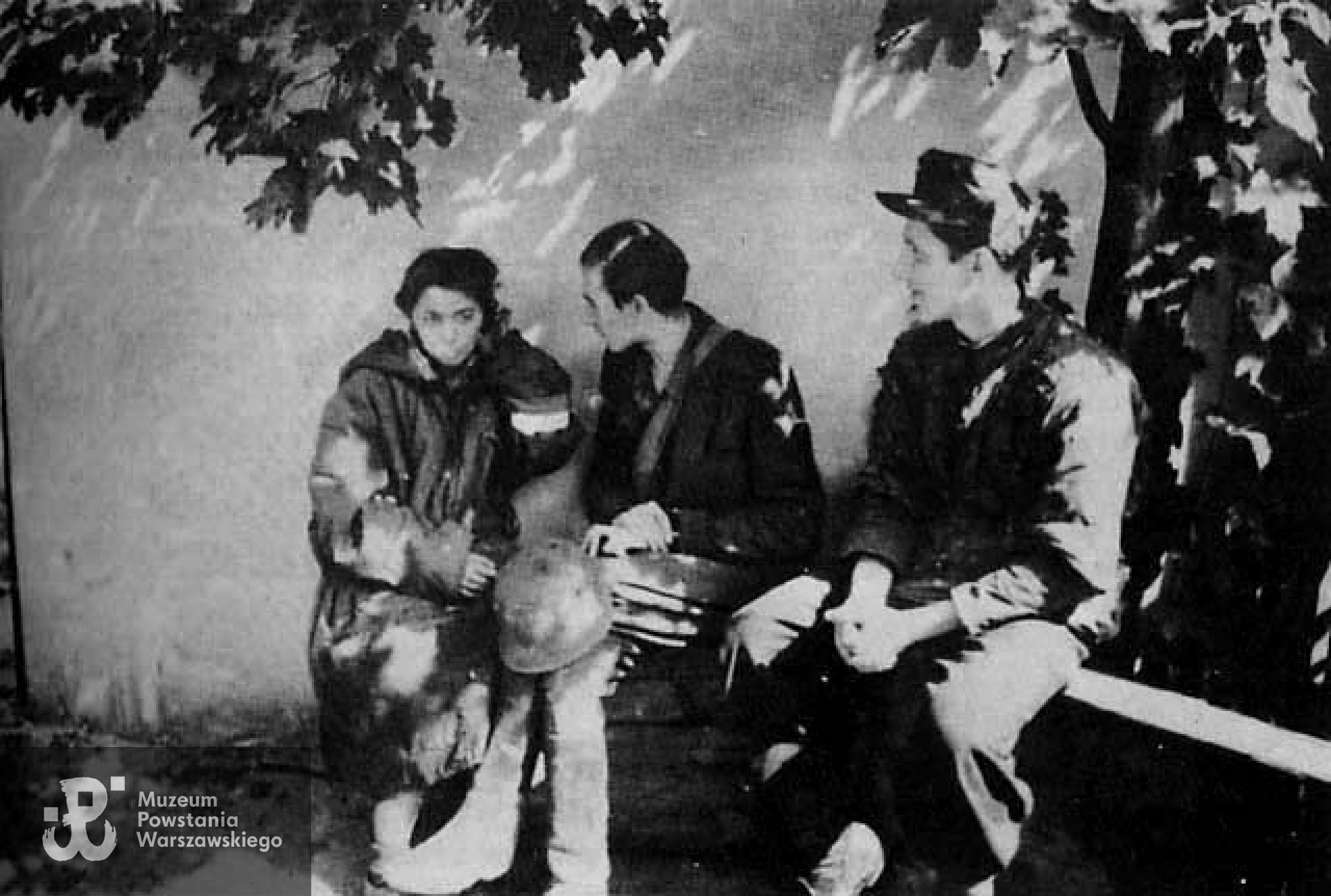 "Iza" z kolegami z "Czaty 49" - ogród w rejonie ul. Wareckiej. Zdjęcie wykonane 2 IX 1944 r., tuż po ewakuacji resztek batalionu kanałami ze Starego Miasta do Śródmieścia. Od lewej siedzą: sanitariuszka "Iza" - Izabela Łucja Wilbik,  strz. "Ulatowski" - Jan Welt i strz. "Kowalski" - Tadeusz Roman