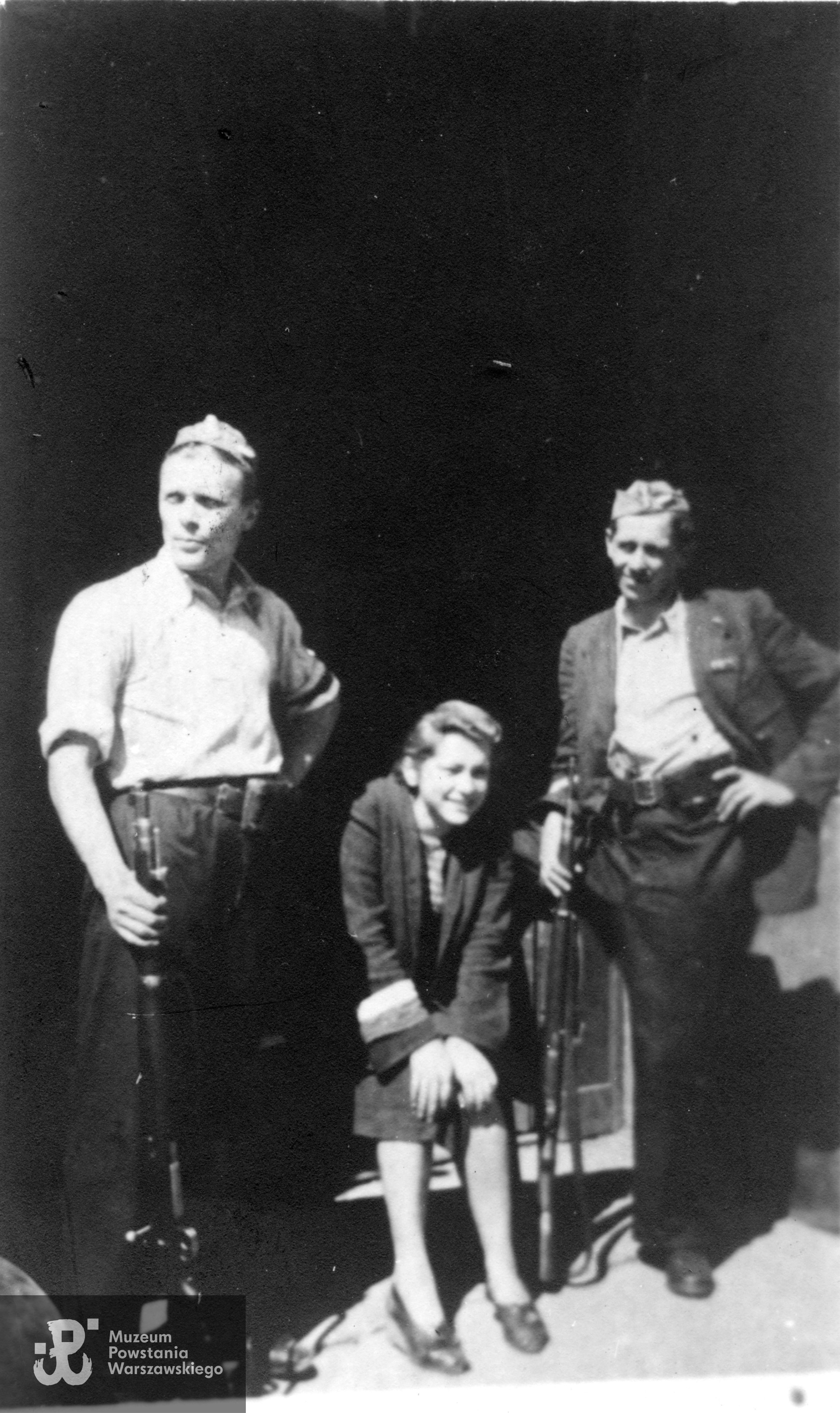 Fotografia z okresu Powstania Warszawskiego przedstawiająca troje Powstańców, pierwszy z lewej Witold Gosławski "Garbaty", z prawej  Zygmunt Biernacki "Sęk" z 3. plutonu Kompanii Ochrony Sztabu "Koszta'". Obaj polegli podczas bombardowania 6 września 1944 roku  pod gruzami kamienicy przy ul. Moniuszki 7. Fot. ze zbiorów Muzeum Powstania Warszawskiego, sygn. MPW-IP/9405 (P/3557).