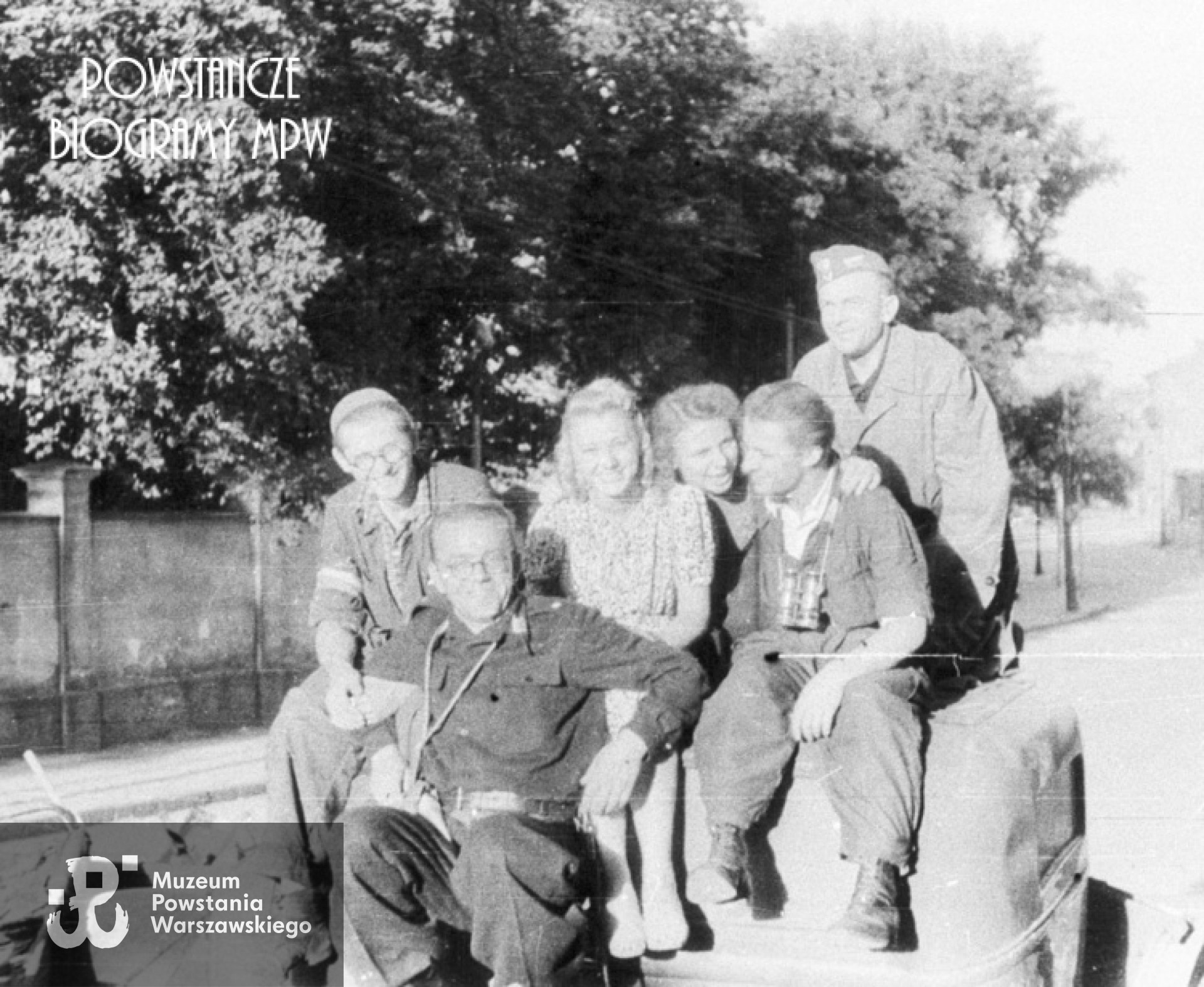 Fotografia z Powstania Warszawskiego. Śródmieście Południowe, ul. Książęca. Barykada z samochodów przecinająca ulicę. Od lewej: pchor. Lech Pudłowski "Leszek", ppor. Henryk Bigajski "Potocki", Daniela Białowąs "Nutka", Wacława Sutowska "Aćka". Stoi pchor. "Korwin". W głębi widoczny mur posesji Książęca 10. Fot. ze zbiorów Muzeum Powstania Warszawskiego, sygn. MPW-IH/5919