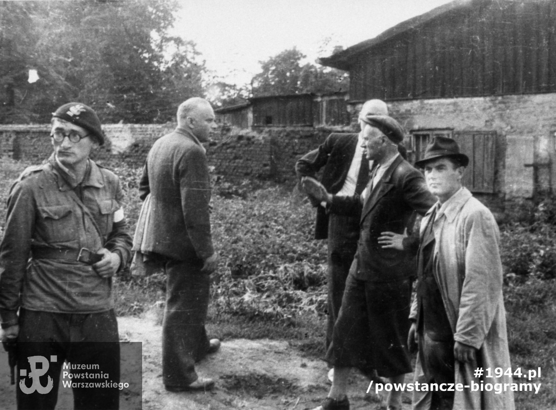 Fotografia z Powstania Warszawskiego. Wola. Godzina "W". Grupa oficerów z dowództwa Batalionu "Pięść" stojąca przy wylocie ul. Długosza na ul. Karolkową oczekuje na koncentrację w rejonie cmentarza ewangelicko-augsburskiego. Od prawej stoją: ppor. Stanisław Bąk "Burza", mjr. Alfons Kotowski "Okoń" dowódca Batalionu, kpt. Felicjan Zawadzki "Fez", kpt. Zbigniew Szarama "Herse" zastępca dowódcy. W tle widoczna południowa część ogrodzenia cmentarza ewangelicko-augsburskiego.  Autorem zdjęcia jest Stefan Bałuk. Ze zbiorów Muzeum Powstania Warszawskiego, sygn. MPW-IH/3407. Prawa autorskie MPW