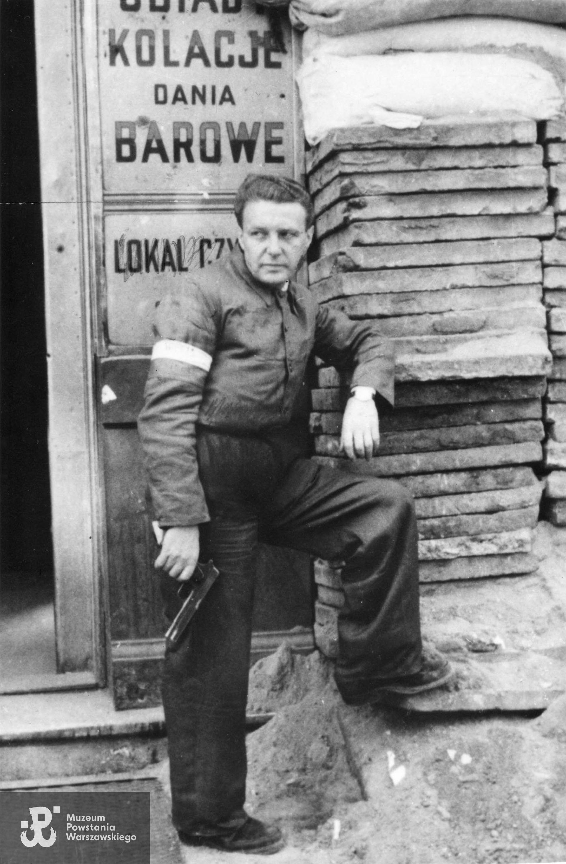Fotografia z Powstania Warszawskiego. Śródmieście Północne. Posterunek powstańczy przed restauracją na ul. Jasnej. Przy barykadzie stoi Edward Krauze „Eka”, „Nałęcz". Fot. ze zbiorów Muzeum Powstania Warszawskiego, sygn. MPW-IK/2206, zbiór Stanisława Kopfa