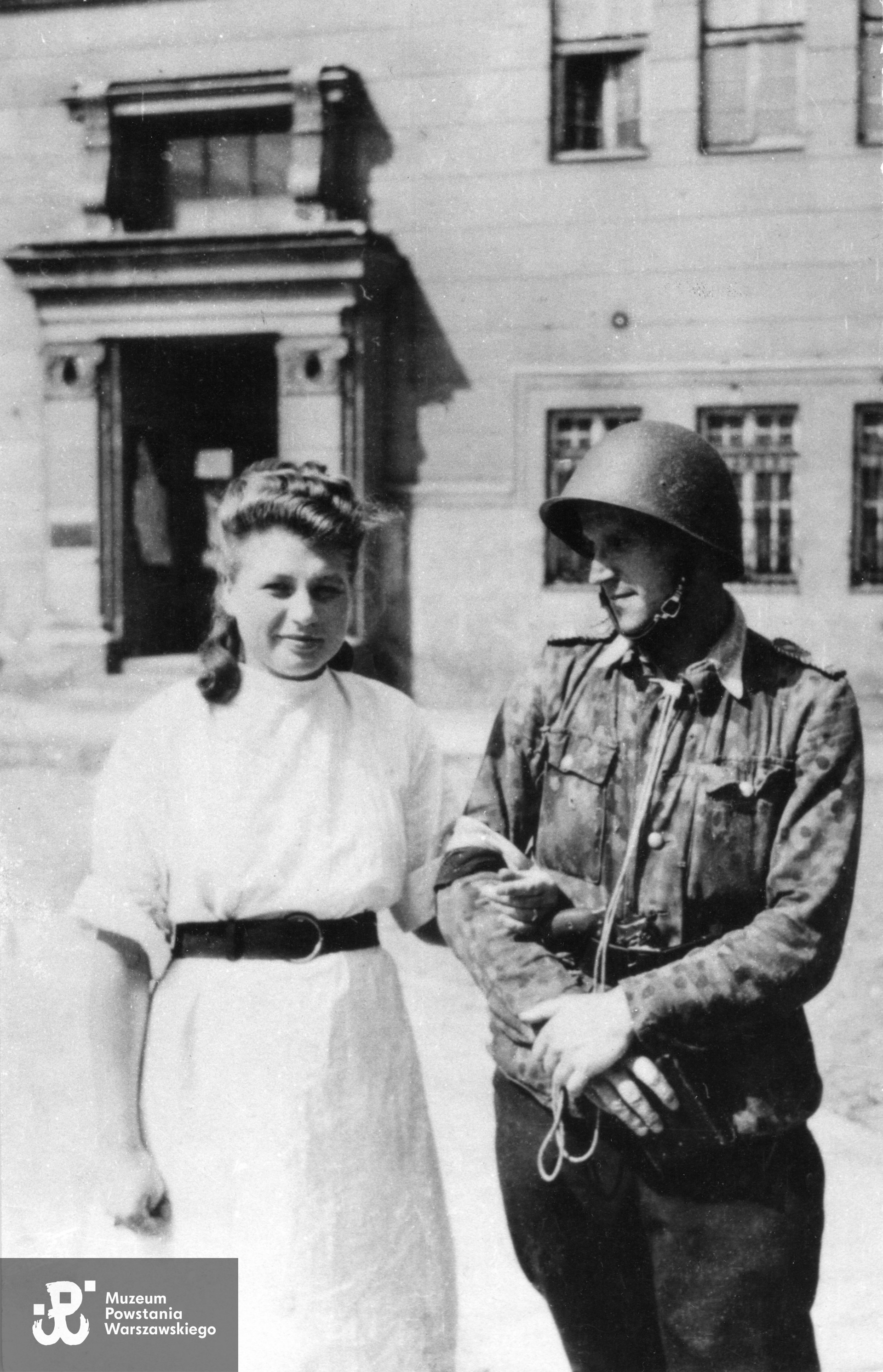 Fotografia z Powstania Warszawskiego. Powiśle. Sanitariuszka Barbara Pieczyrak "Bojanowska" (po mężu Rygiel) i kpr. pchor. Jerzy Małko Wyganowski", oboje z 109 plutonu 2. kompanii Grupy Bojowej "Krybar", przed szpitalem polowym na ulicy Konopczyńskiego 3/5. W tle wejście do budynku Gimnazjum Męskiego przy ul. Konopczyńskiego 4-4A. Fot. ze zbiorów Muzeum Powstania Warszawskiego, sygn. MPW-IK/1520