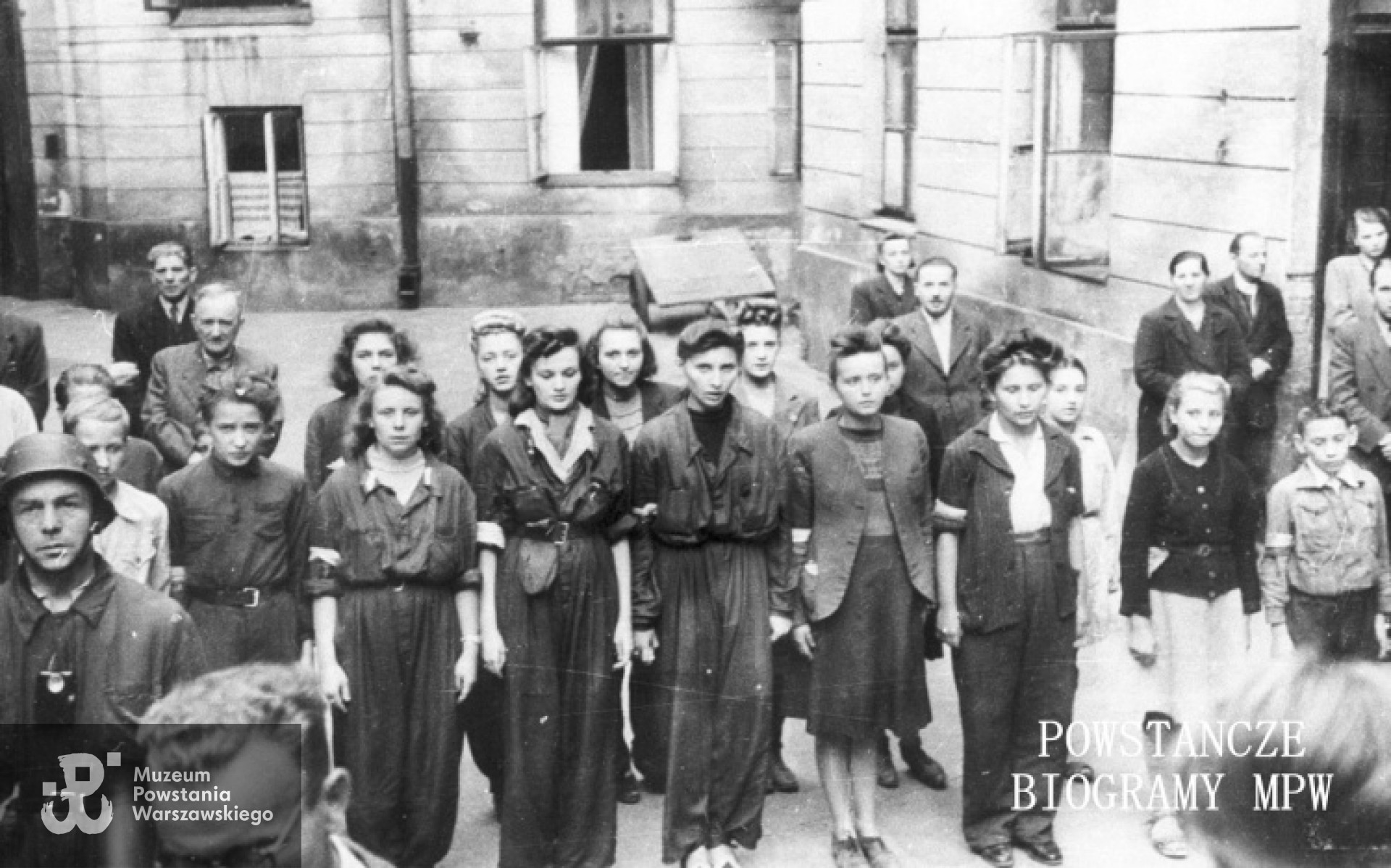 Szersze ujęcie. Sanitariuszki z 1. plutonu "Kłosa" 3. kompanii "Redy" batalionu "Miłosz" podczas mszy na podwórzu kamienicy.  W środku rzędu Hanna Baranowska "Lalka". Autorem zdjęcia jest Wojciech Marczyński "Bogusław".  Fot. ze zbiorów Muzeum Powstania Warszawskiego, sygn. MPW-IH/5916