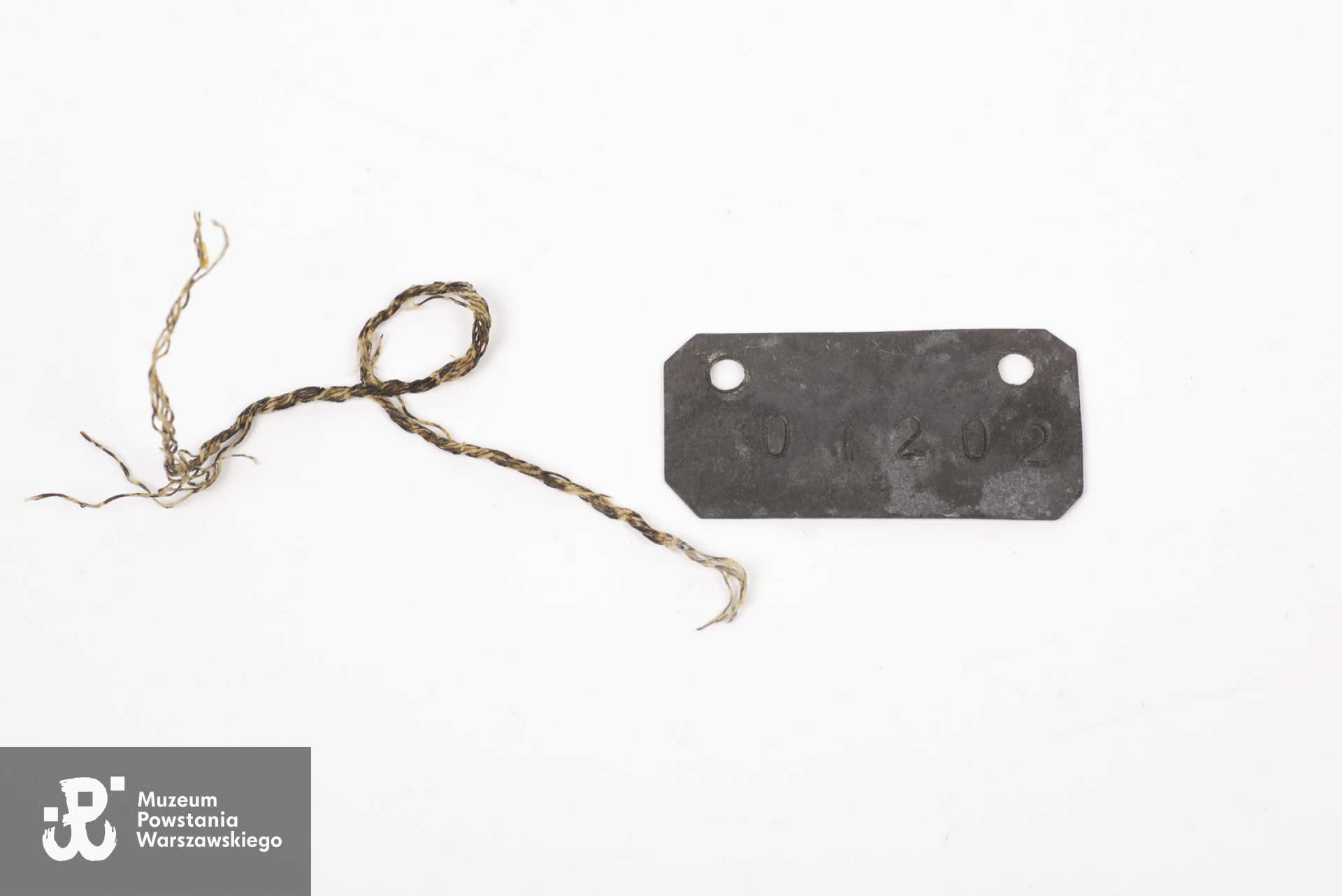 Metalowy nieśmiertelnik nr 01202 noszony na piersi przez do kpt. Władysława Klęka ,oficera Armii Krajowej skazanego na śmierć przez sąd wojskowy SS w niemieckim obozie jenieckim Sandbostel.  Zbiory Muzeum Wojska Polskiego w Sydney