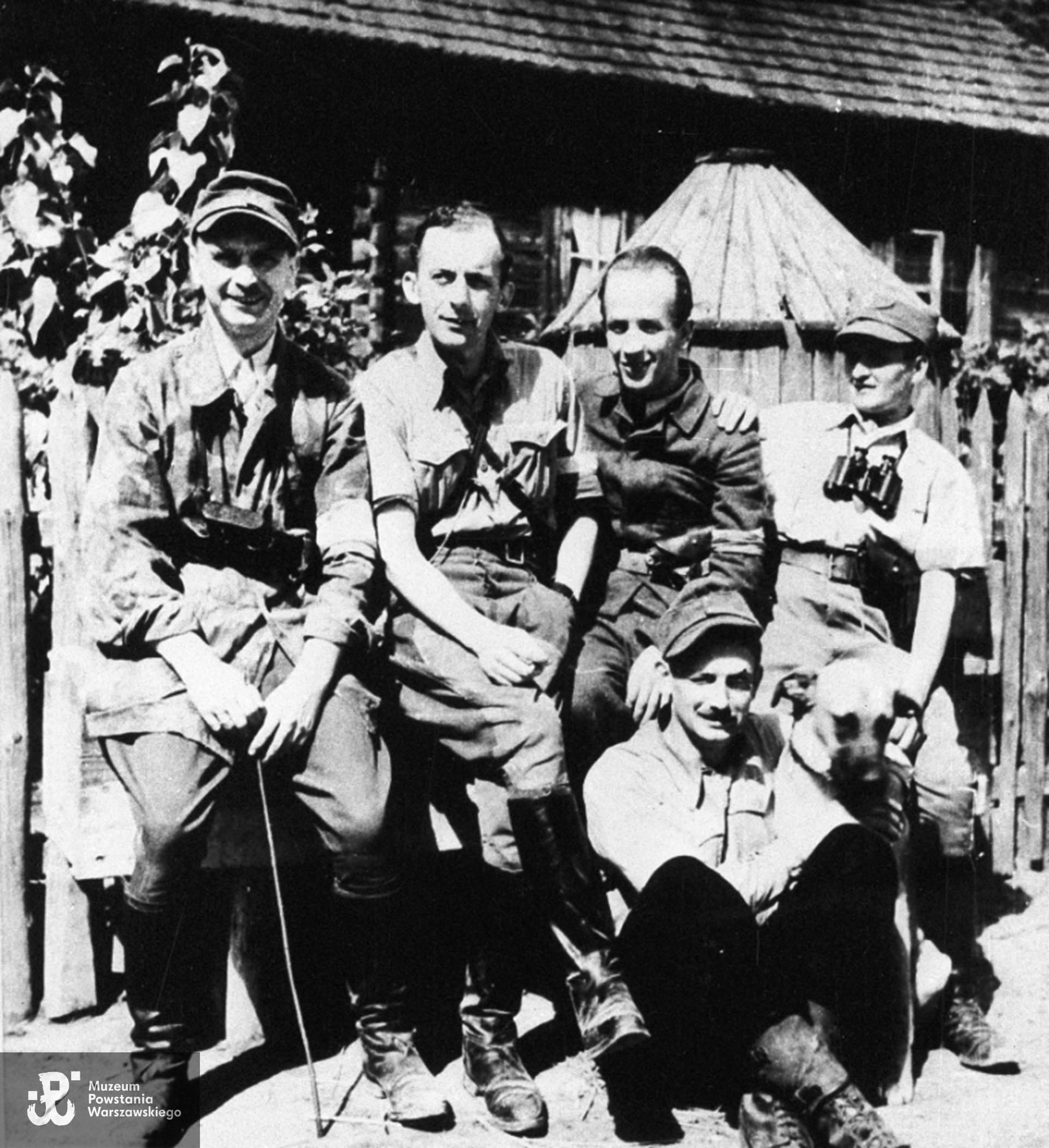 Fotografia z Powstania Warszawskiego. Lasy Chojnowskie, Powstańcy z Ochoty, obrońcy Reduty Kaliskiej: ppor. Józef Winiarski "Prostak", por. Andrzej Chyczewski "Gustaw", ppor. Stanisław Kamiński "Kret", sierż. Jan Wieczorek "Bimber", siedzi ppor. Janusz Antoszek "Antoś". Fot. ze zbiorów Muzeum Powstania Warszawskiego, sygn. MPW-IH/5300.