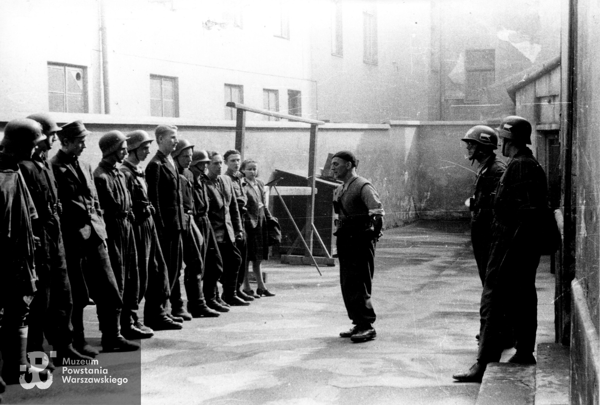 Fotografia z Powstania Warszawskiego. Śródmieście Południowe, ul. Książęca. Zbiórka drużyny wypadowej 1. plutonu "Kłosa" 3. kompanii "Redy" batalionu "Miłosz" na podwórzu kamienicy przy ulicy Książęcej 23. Od lewej: kpr. pchor. Stanisław Szabłowski "Witeź", sierż. pchor. Juliusz Pietrzykowski "Teddy", łączn. Leszek Piotrowski "Tygrys", strz. Witold Hermanowski "Świt", strz. Jerzy Ryszard Rosiak "Pantera", st. strz. Ryszard Zieliński (?) "Desant", strz. Stanisław Białowąs "Jajko", NN, NN, NN, strz. Zofia Tomasik "Teresa". Przed frontem oddziału por. Marian Stasiak "Czółno", za nim ppor. Henryk Bigajski "Potocki" i NN. Autorem zdjęcia jest Wojciech Marczyński "Bogusław". Fot. ze zbiorów Muzeum Powstania Warszawskiego, sygn. MPW-IS/819 (P/8598/16).