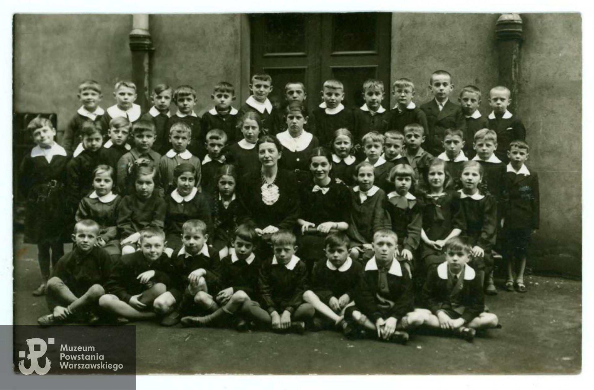 Fotografia wykonana w roku szkolnym 1938/1939 przedstawiająca uczniów klasy II B ze 171. Publicznej Szkoły Powszechnej przy ul. Hożej 13. Na zdjęciu widoczni m. in. późniejsi harcerze Szarych Szeregów:  Benedykt Piwnicki (w pierwszym rzędzie, siedzący drugi od lewej), Zdzisław Żukowski (w trzecim rzędzie trzeci z lewej), Eugeniusz Kłos (w ostatnim rzędzie na tle drzwi, siódmy od lewej), Tadeusz Różycki "Dudek" (w ostatnim rzędzie pierwszy z prawej). W środku siedzi wychowawczyni, polonistka, pani Helena Sewerynowa. Fot. z archiwum rodzinnego Tadeusza Różyckiego.