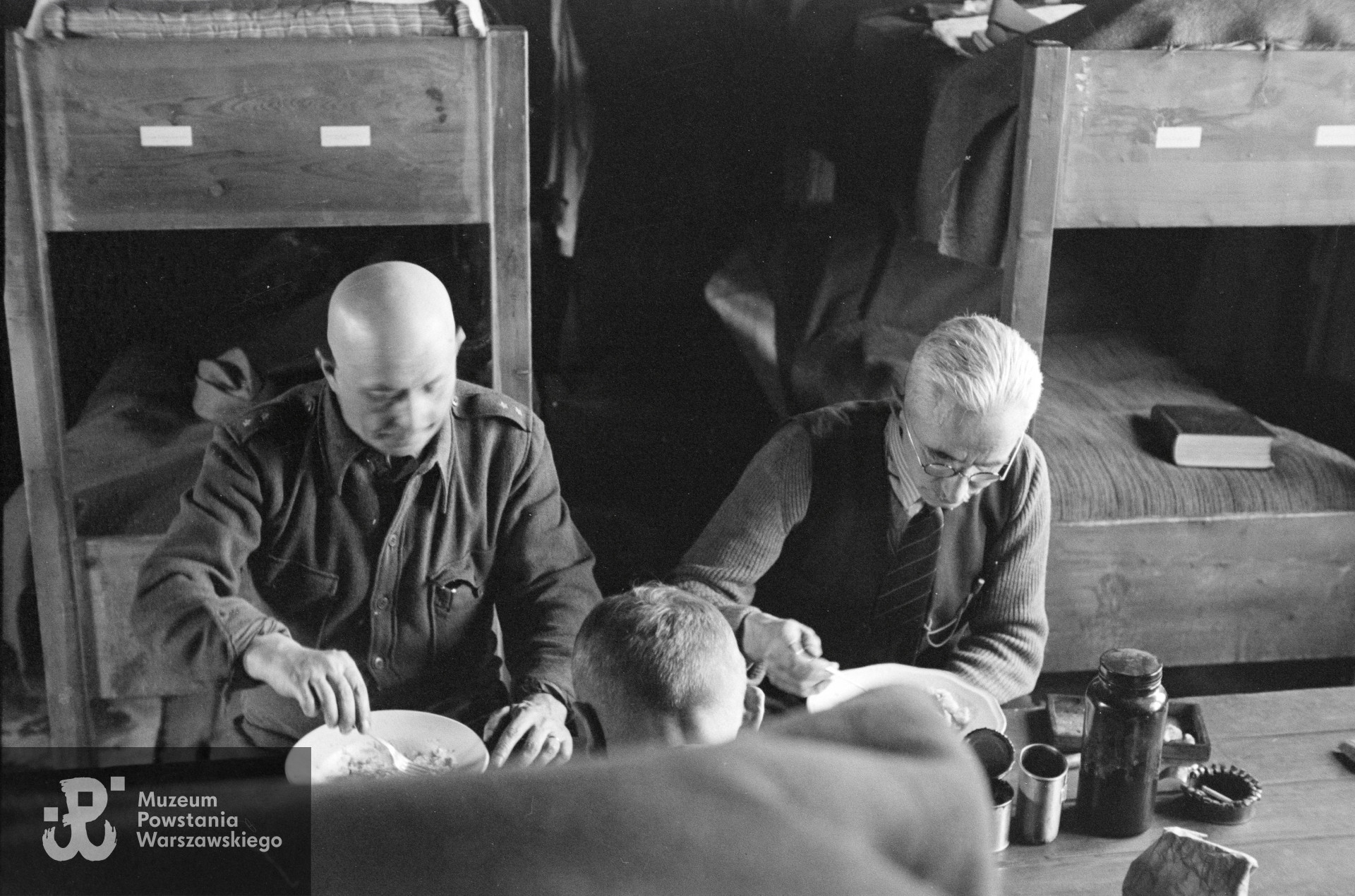 Fotografia z Polskiego Szpitala Wojskowego w saksońskim Zeithain.  Wnętrze baraku nr 14 .Por. Jan Sawczuk „Knihinicki Jan” (z lewej) i mjr dr Tadeusz Kawecki „Lwowicz” przy posiłku. Autorem zdjęcia jest Czesław Gerwel „Orłoś”. Fot. ze zbiorów Muzeum Powstania Warszawskiego, sygn. MPW-IN/3826