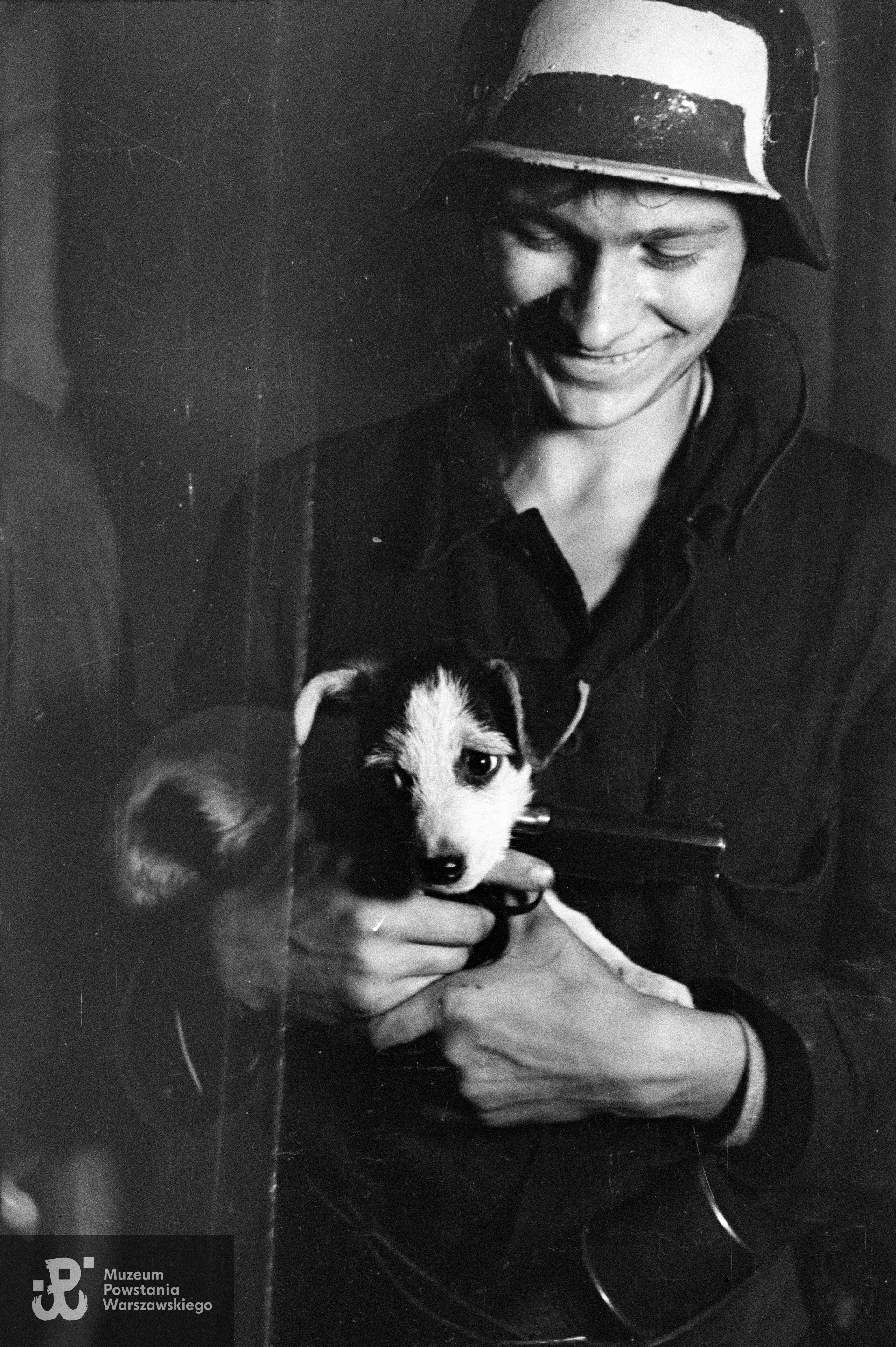 Fotografia z Powstania Warszawskiego. Śródmieście Północne. Plut. Wacław Latoszek "Kukułka" z Oddziału Osłonowego Wojskowych Zakładów Wydawniczych (WZW) z pistoletem VIS wz. 1935 i psem Kropką na kwaterze w kamienicy Lewenfisza przy pl. Napoleona 1 róg Boduena 2, róg Sienkiewicza. Fot. ze zbiorów Muzeum Powstania Warszawskiego, sygn. MPW-IN/222. 