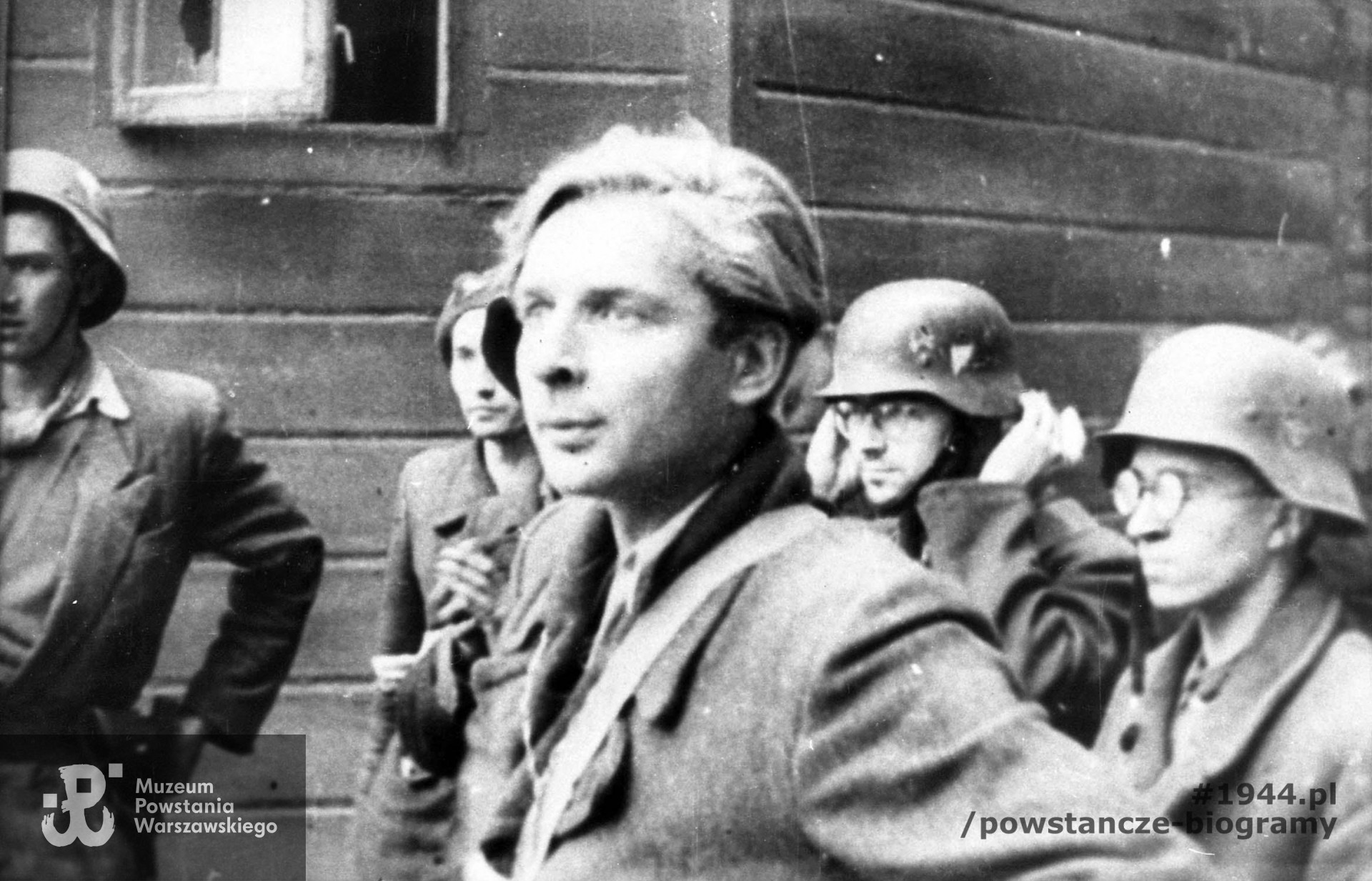 Fotografia filmowa z Powstania Warszawskiego. Śródmieście Północne. Powstańcy plutonu "Rygla" z 4 kompanii Zgrupowania "Bartkiewicz" na dziedzińcu zdobytej Komendy Policji przy ul. Krakowskie Przedmieście 1. W środku na pierwszym planie strz. Wiesław Nałęcz-Mroczkowski "Wiesiek", za nim od prawej st. strz. Zbigniew Kurbiel "Krakus", st. strz. pchor. Józef Sowilski "Bohdan" (poprawia hełm). Ze zbiorów Muzeum Powstania Warszawskiego, sygn. MPW-IH/1462