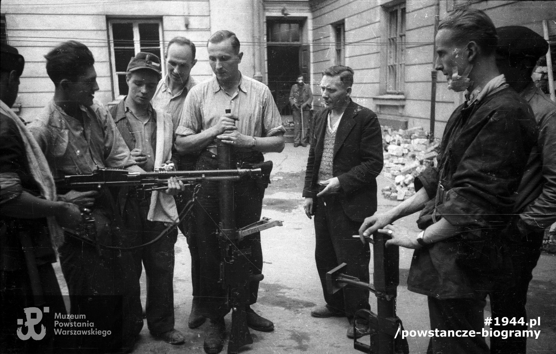  Podwórze domu przy ul. Świętokrzyskiej 20. Kpr. pchor. Włodzimierz Wiśniewski "Cygan" z kompanii "Janusza" z batalionu "Harnaś" pokazujący kolegom czechosłowacki ręczny karabin maszynowy ZB wz. 1926 zdobyty po ataku na Komendę Policji. W środku stoi plut. pchor. Adam Podkóliński "Michał", „Olszewski” (w jasnej koszuli) z opartym o ziemię niemieckim lekkim karabinem maszynowym leMG 08/15. Powstaniec na pierwszym planie po prawej trzyma brytyjski granatnik przeciwpancerny PIAT. Fot. ze zbiorów Muzeum Powstania Warszawskiego, sygn. MPW-IN/10211. Autorem zdjęcia jest Joachim Joachimczyk "Joachim"