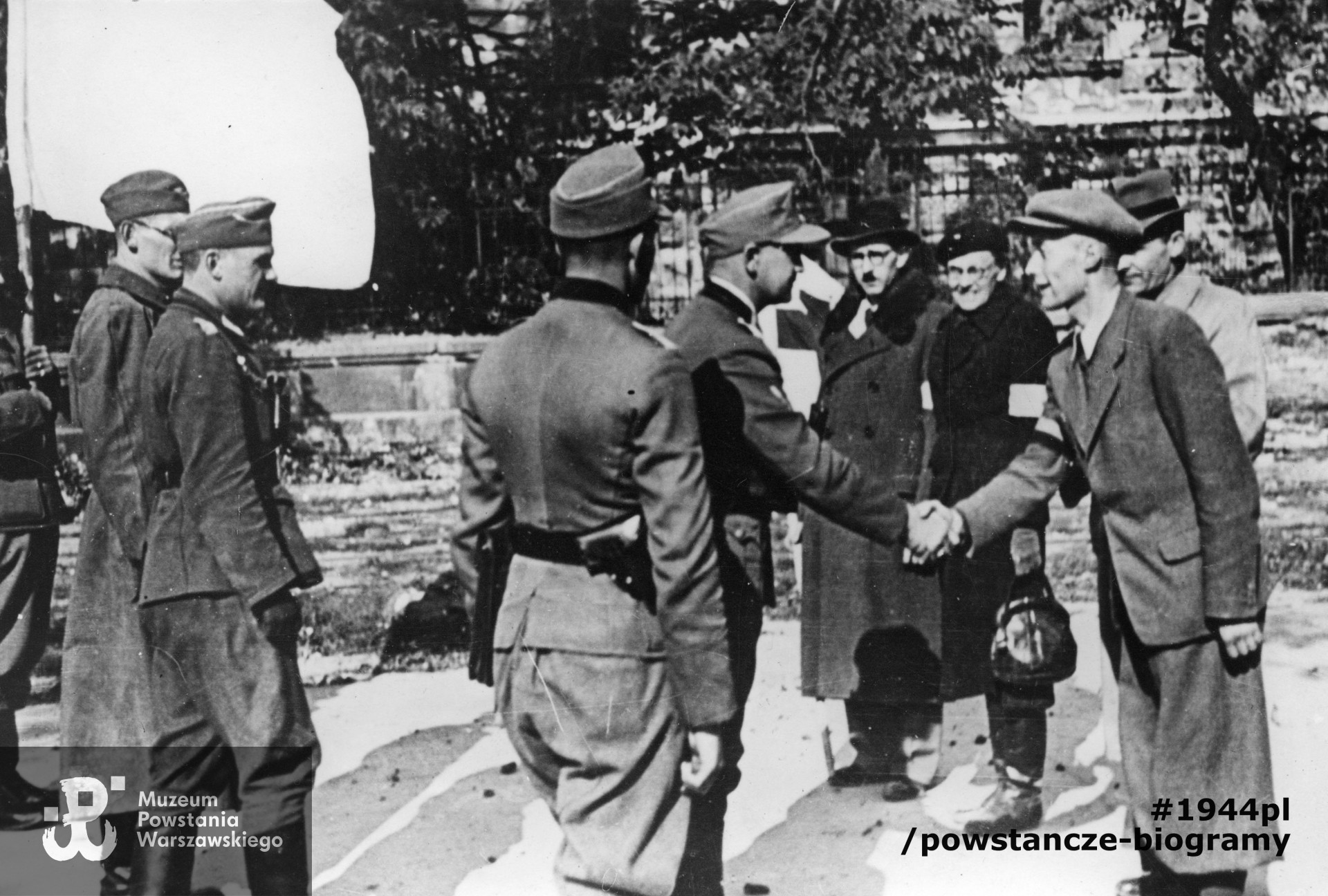 Fotografia z Powstania Warszawskiego. Śródmieście Południowe. Parlamentariusze polscy na ulicy 6 Sierpnia (obecnie Nowowiejska) witający się z delegacją niemiecką przed pertraktacjami w sprawie kapitulacji Powstania. W tle gmach Politechniki Warszawskiej. Po prawej stronie przedstawiciele Polskiego Czerwonego Krzyża - Maria hrabina Tarnowska i dr Hieronim Bartoszewski (w okularach i czarnym kapeluszu). Fot. ze zbiorów Muzeum Powstania Warszawskiego, sygn. MPW-IP/8656