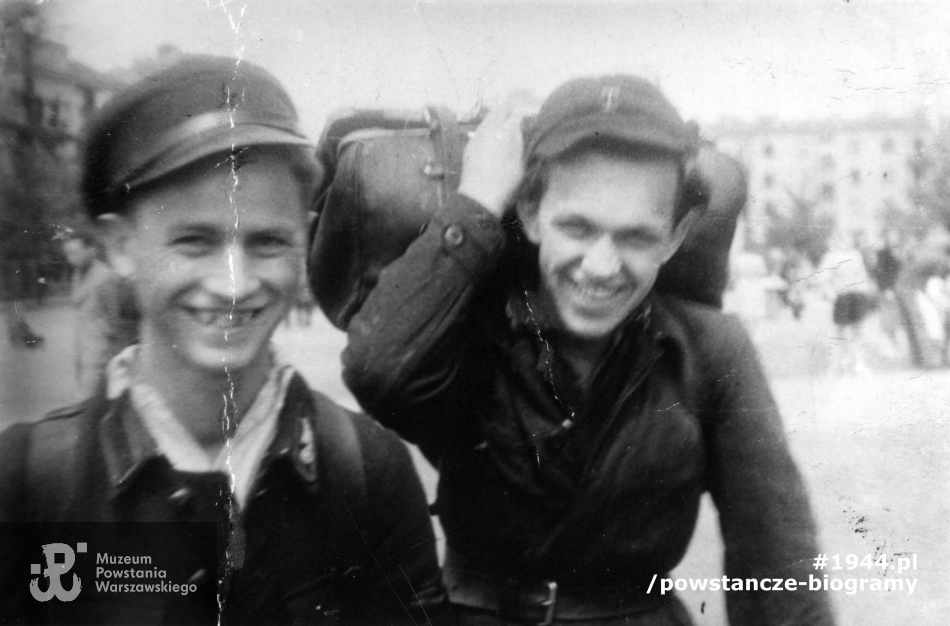 Fotografia z okresu okupacji niemieckiej w Warszawie. Strz. Stanisław Małoszczyk "Ignaś"(po lewej) i kpr. pchor.  Wiktor Dowalla  z praskigo Kedywu DB-22 na ul. Otwockiej podczas transportu broni do lokalu konspiracyjnego. Ujęcie w kierunku północnym. W tle od prawej kamienica przy ul. Łochowskiej 44 i po lewej jeden z budynków szkoły przy ul. Otwockiej 3. Fot. ze zbiorów Muzeum Powstania Warszawskiego, sygn. MPW-IK/387 - zbiór Stanisława Kopfa ps. "Malarz"